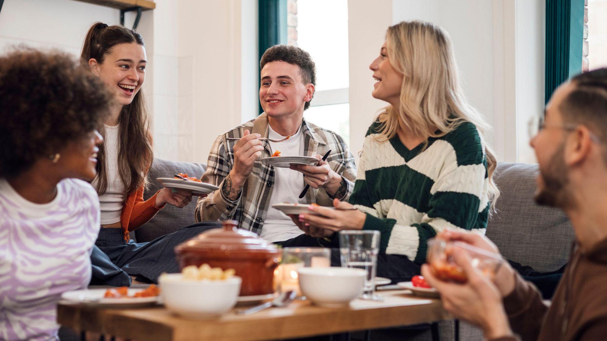 A group of students share a meal around a coffee table. 