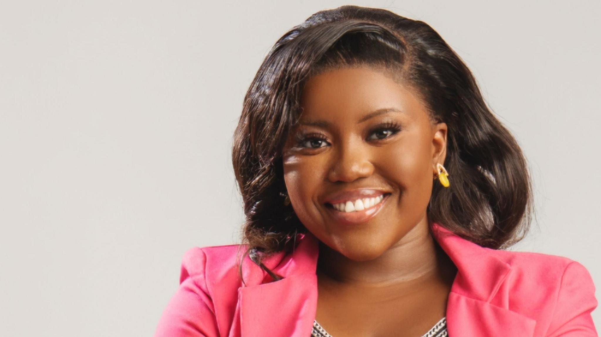 A woman wearing a pink blazer smiles for the camera.