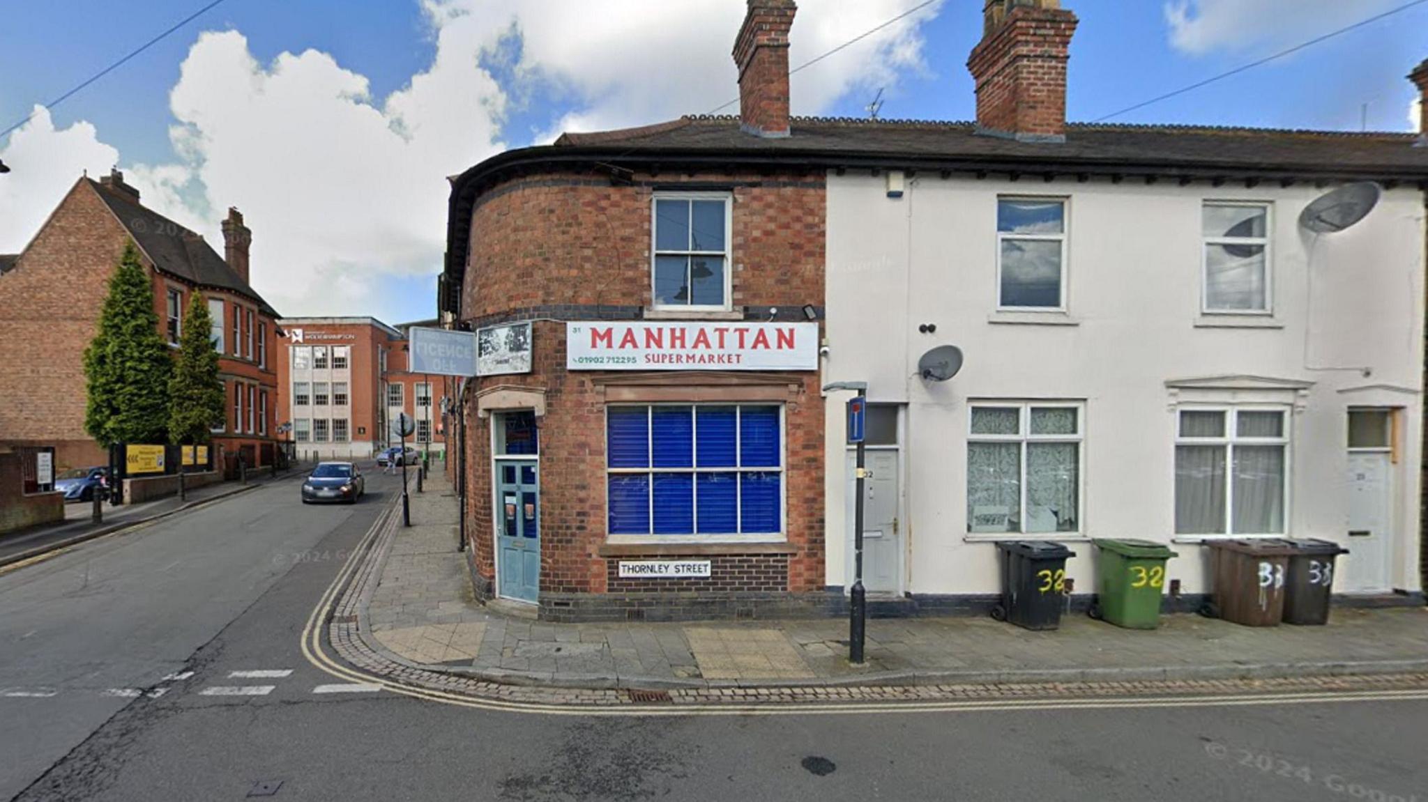 A corner shop with a light blue door. A white sign spells out MANHATTAN in red letters