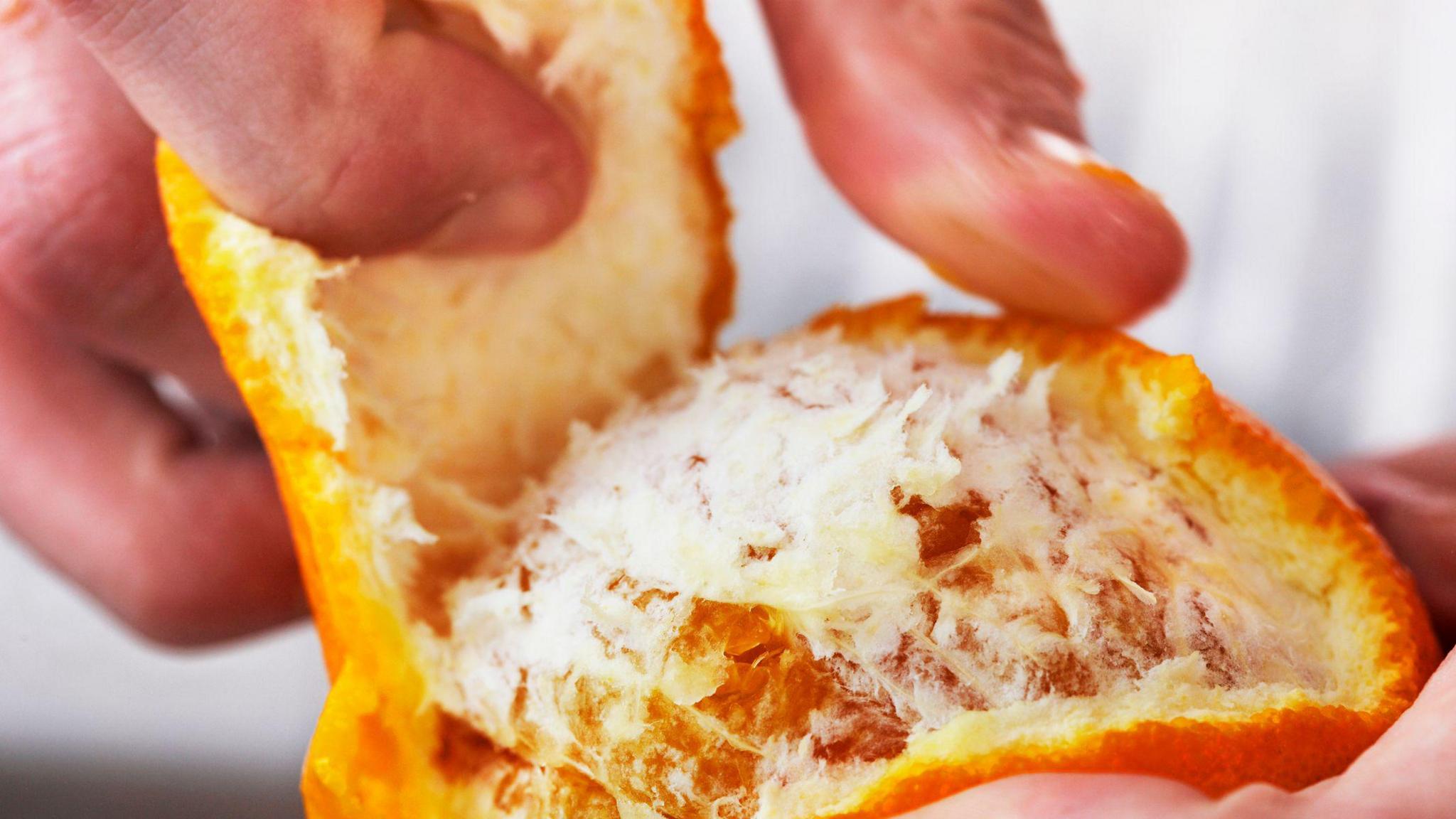 Close up of fingers peeling the skin of an orange revealing the fleshy fruit underneath