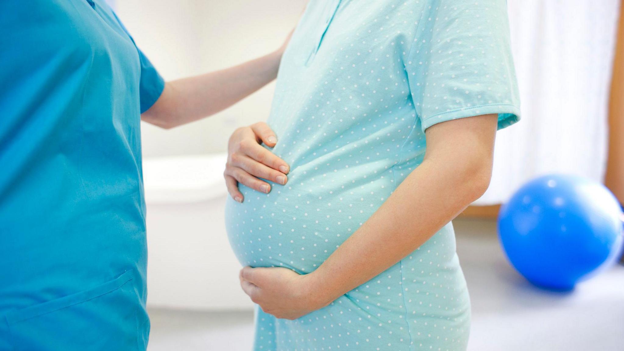 A woman cradling her womb, with another woman standing to her left putting her arm on the lady's shoulder