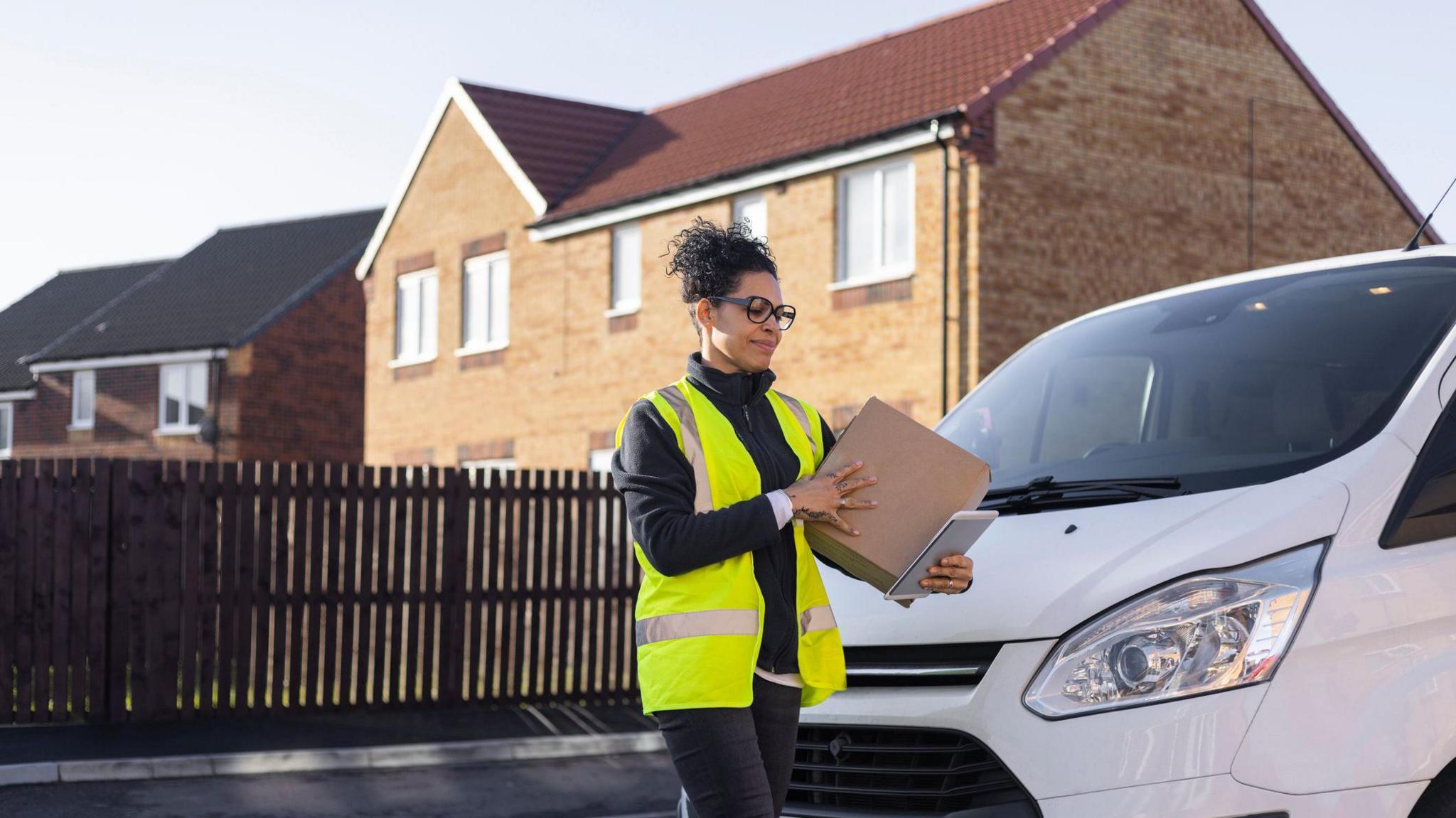 A delivery worker carrying a parcel out of their white delivery van.