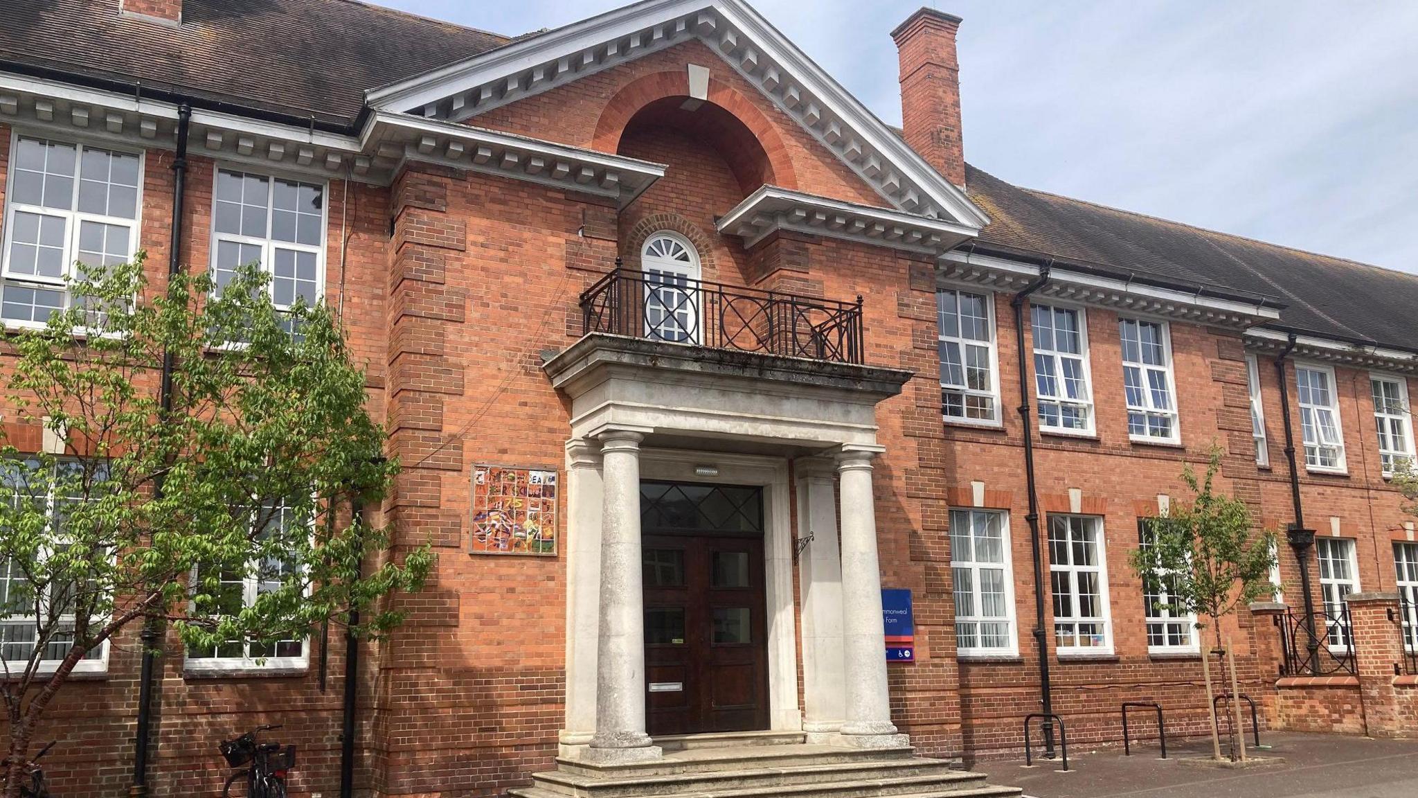 Front of one of the school buildings - a traditional large red brick building with pitched roof, large windows and a grand entrance with pillars