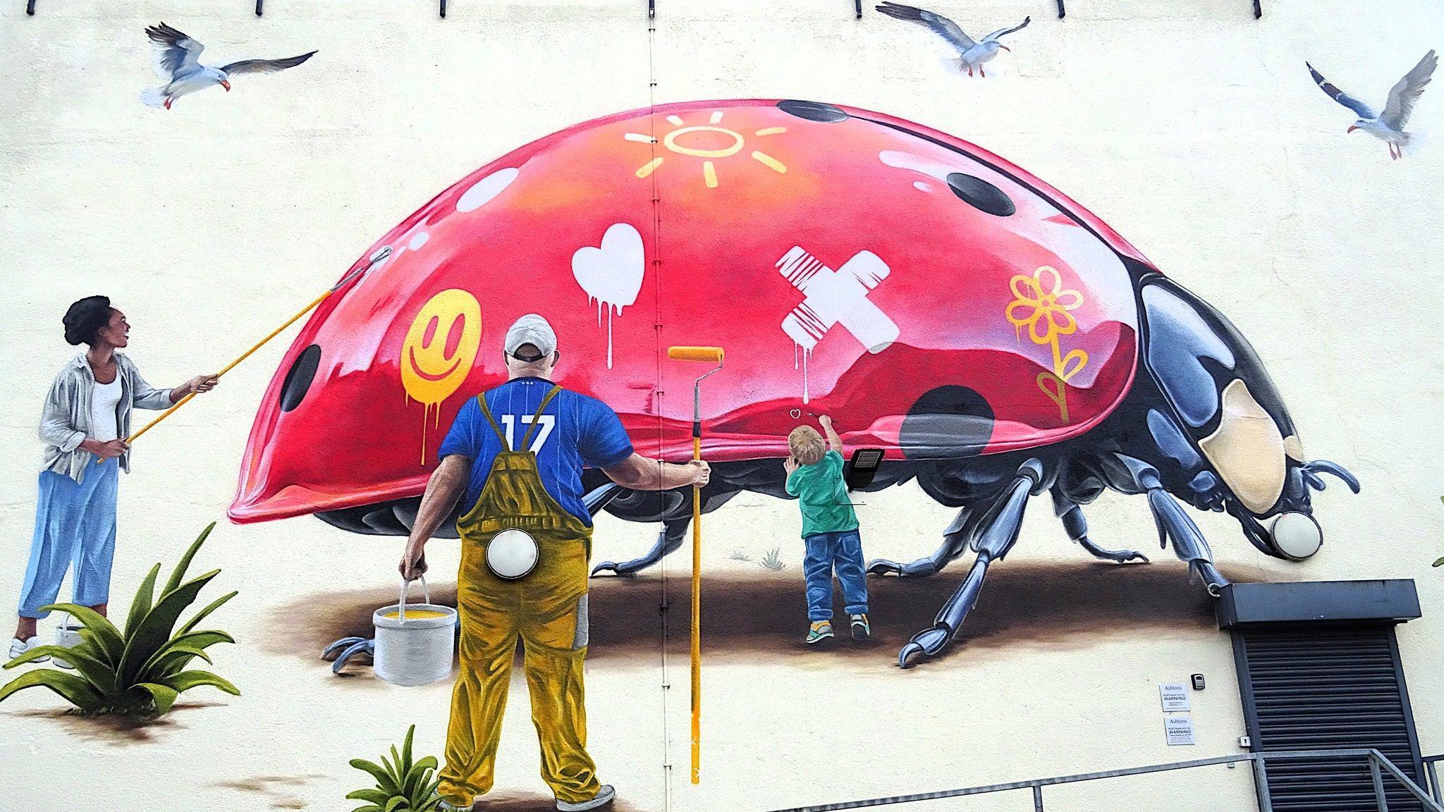 One of the large-scale murals that has already been painted in Ipswich by London-based artist Woskerski. It depicts a ladybird that is missing some of its black spots which members of the community are painting onto it showing community spirit.