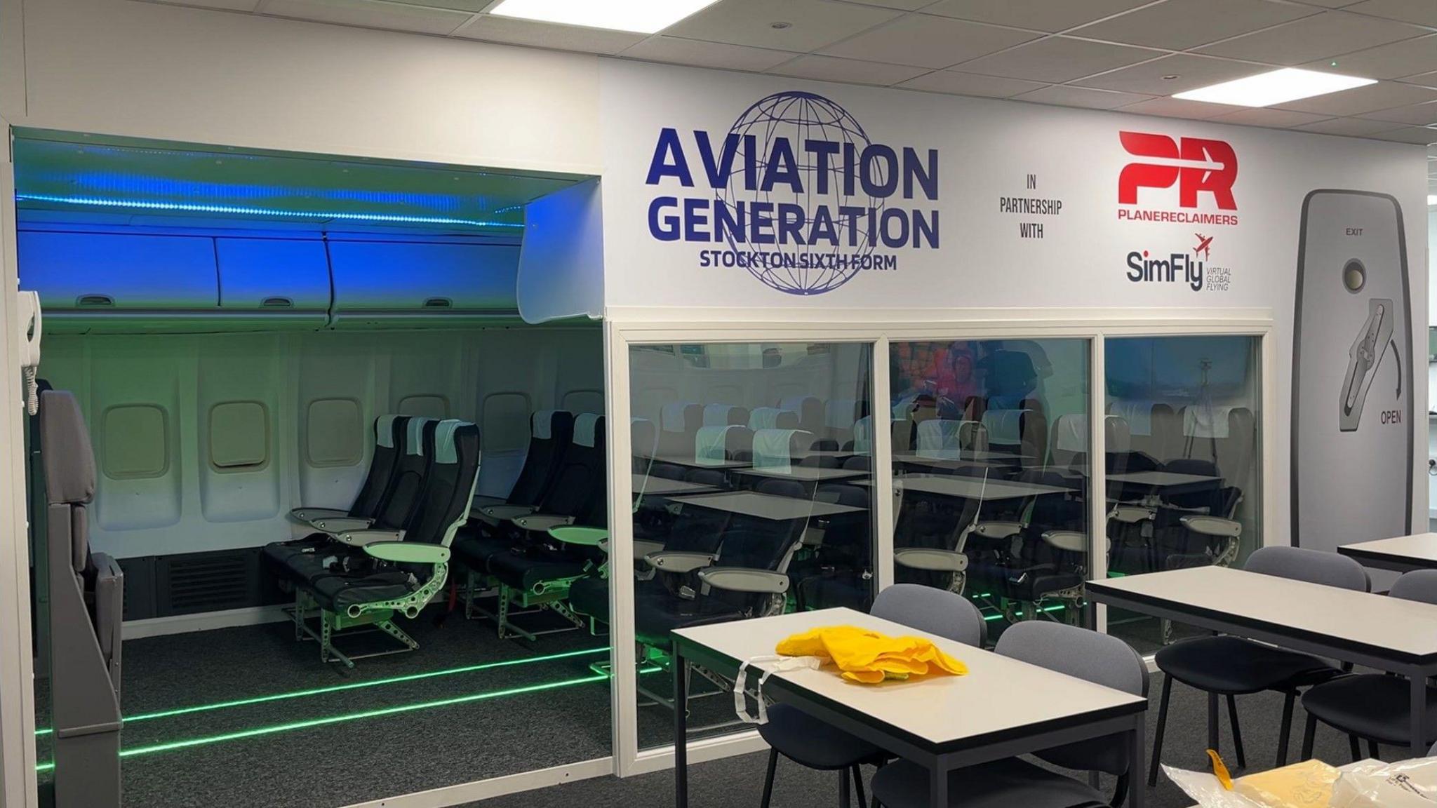 A classroom with tables and chairs and a replica boeing cabin behind with an aisle of seats with plane windows. Above the entrance can be read: "Aviation Generation Stockton Sixth Form.