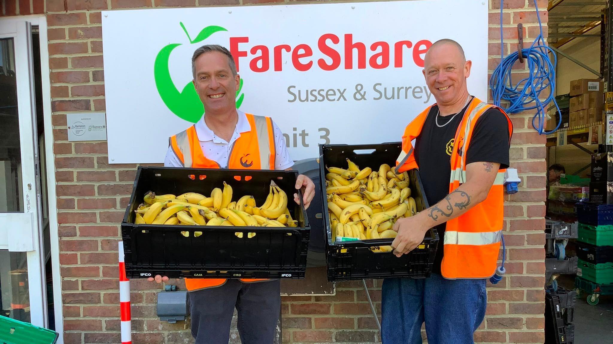Two men hold big boxes of bright yellow bananas