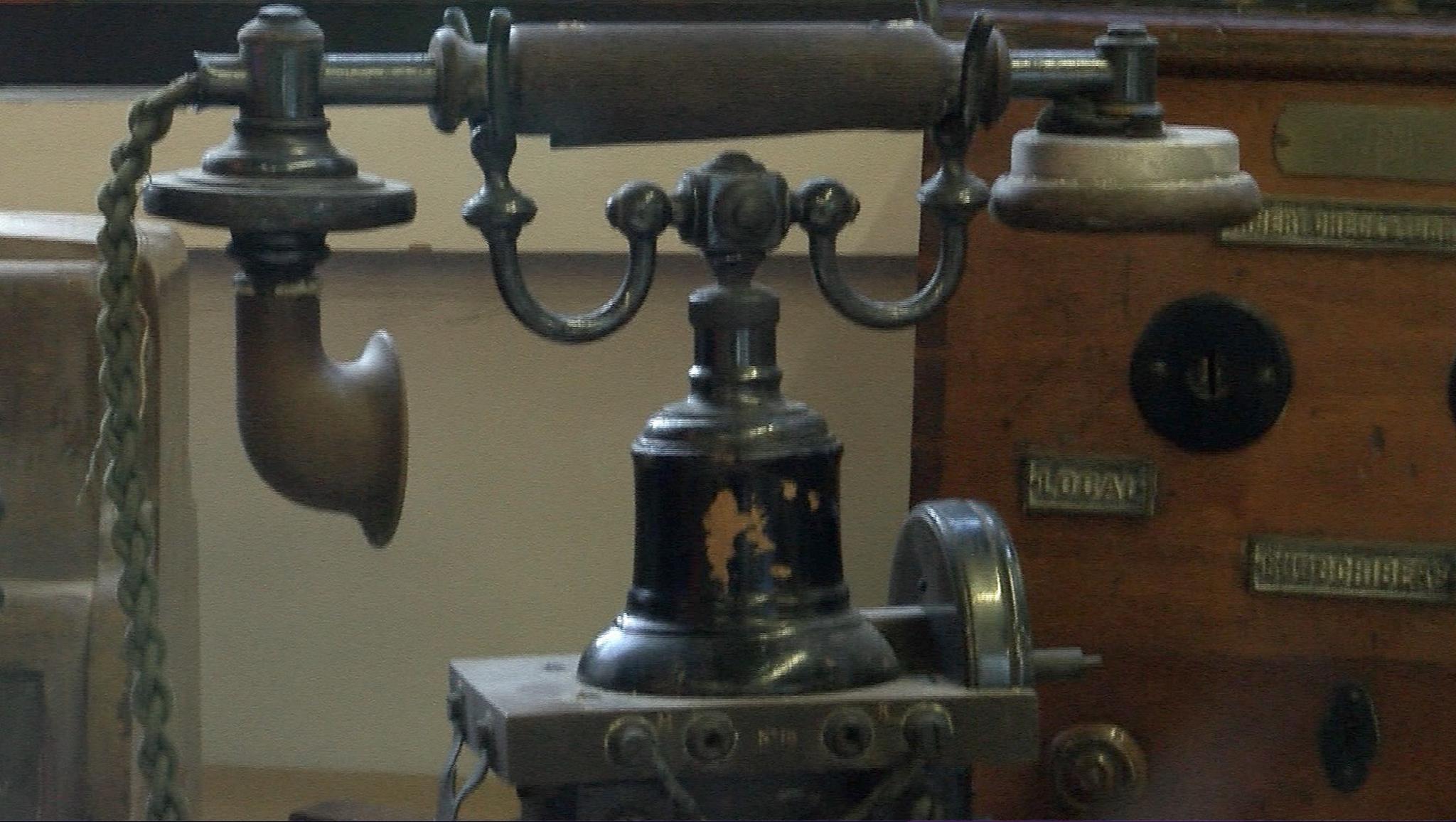 An early 20th-century telephone, known as the "Eiffel Tower" because of its ornate design, has a brass, horn-style receiver resting on a black, bell-shaped body.