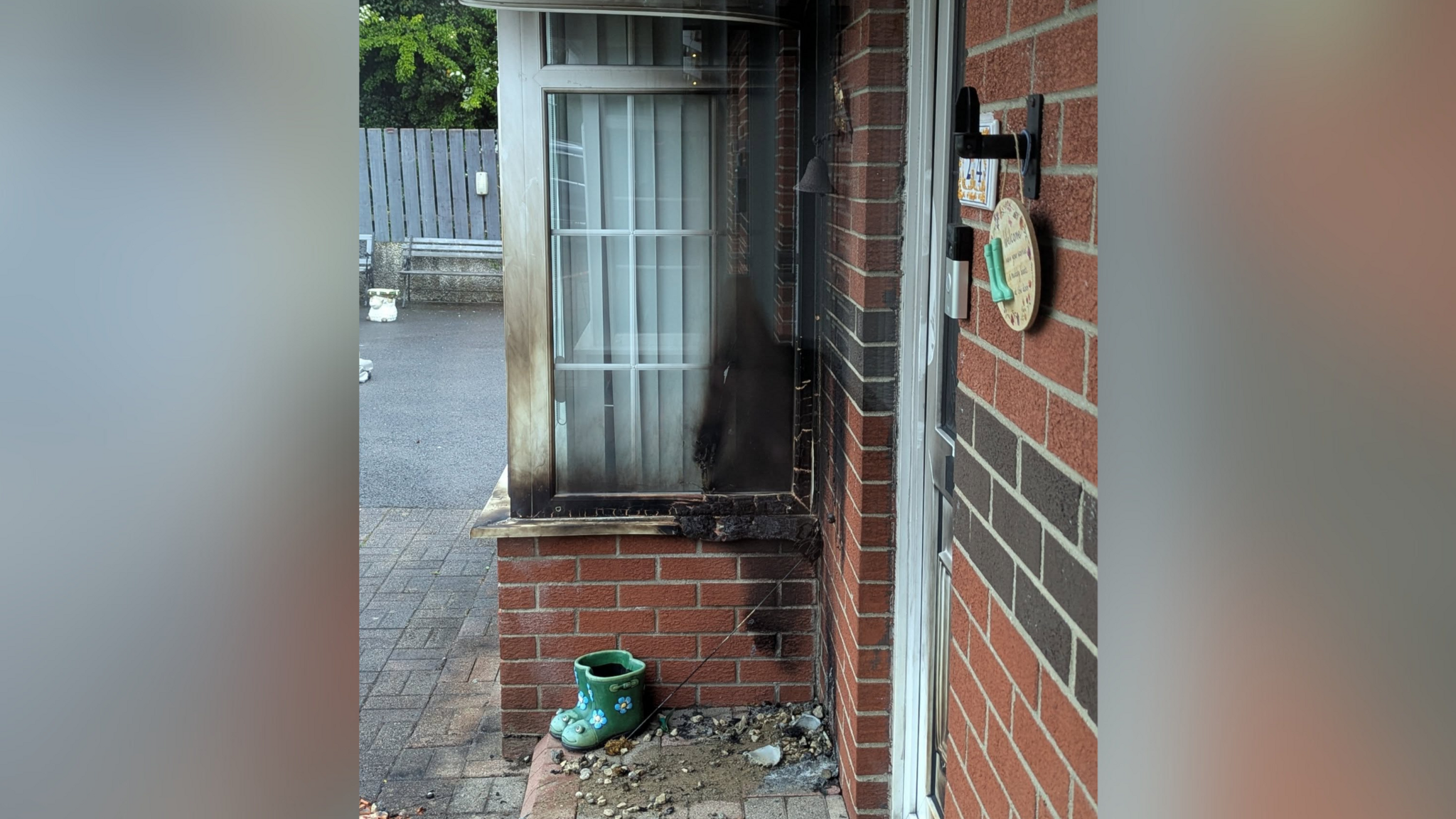 The porch of a home, with red brick walls, with black soot along the window and rubble on the ground.