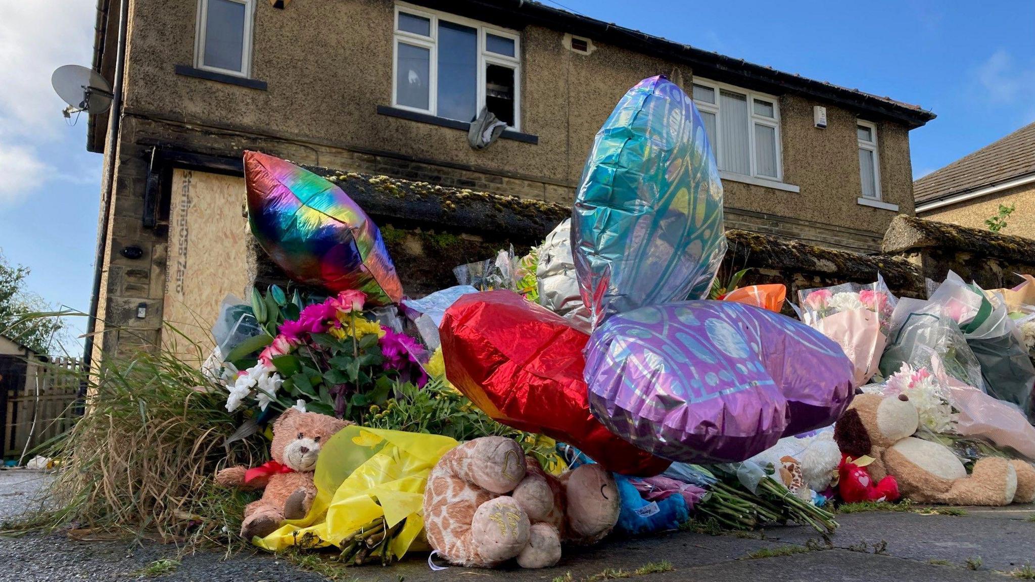 Cuddly toys and bunches of flowers outside the house where a mum died and her three children were fatally injured 