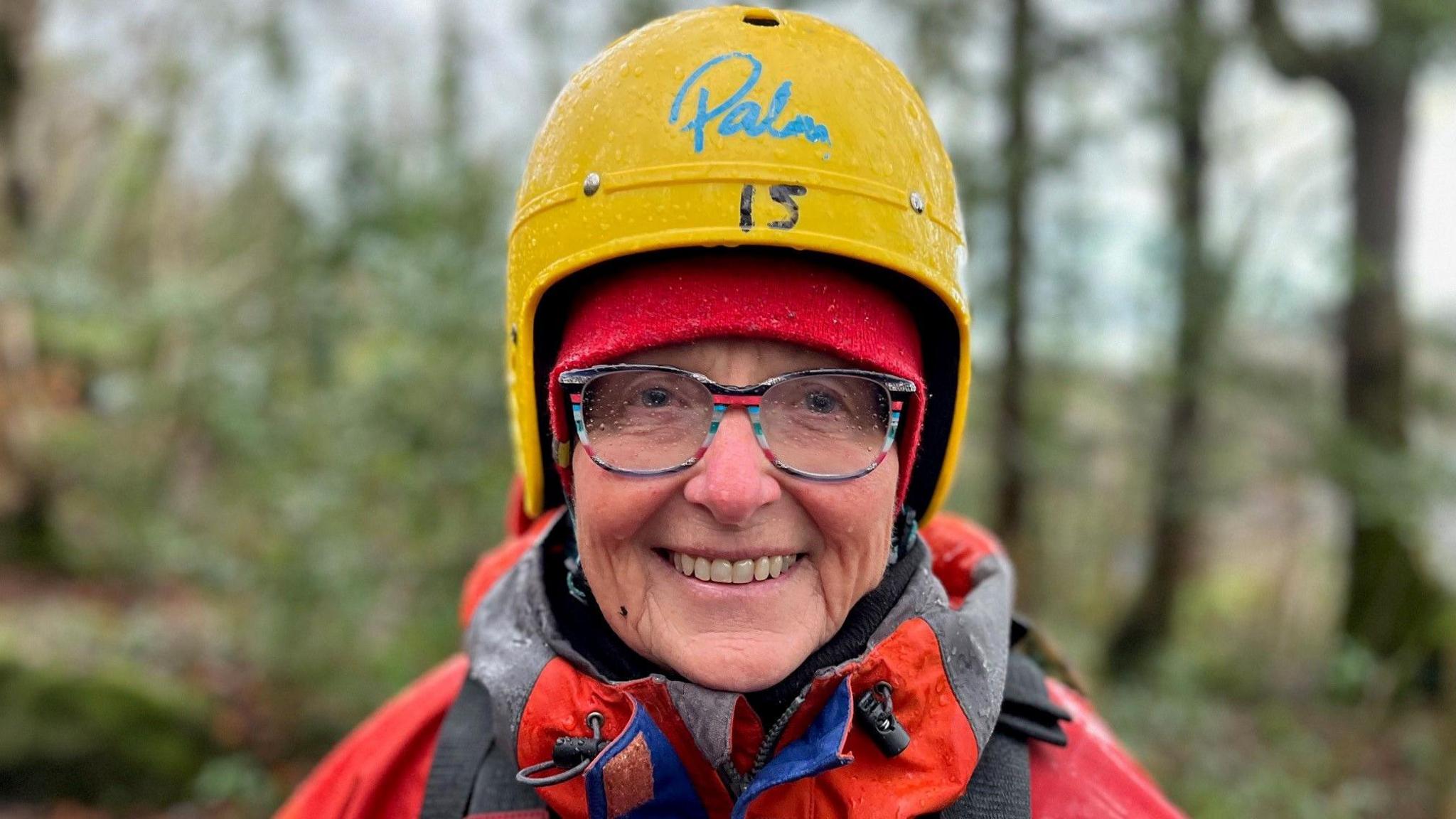 Karen Humphries smiling at the camera. She is wearing bright red protective clothing, lifejacket and helmet, to keep her safe while gorge-walking.