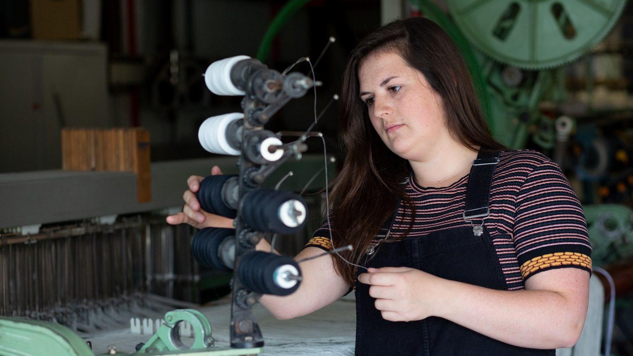 A woman with dark brown hair studies various threads as she weaves them together using a machine