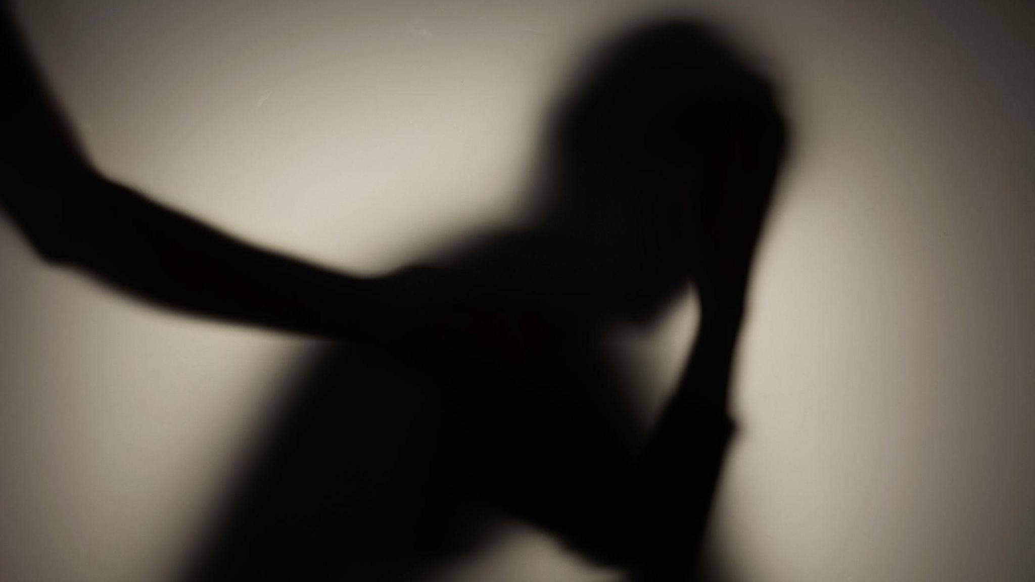 A silhouette of a sitting person with their head in their hands. Someone else has their hand on the sitting person's shoulder.