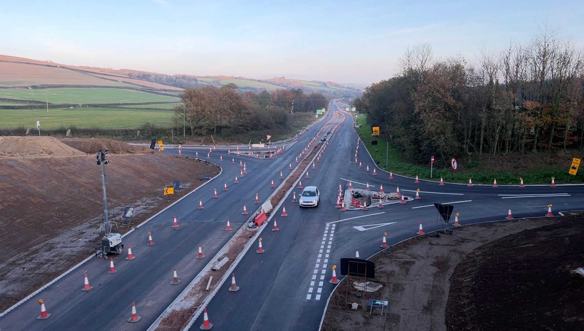 Ongoing works on the North Devon Link Road with a car travelling towards the camera and traffic cones lining the roads.