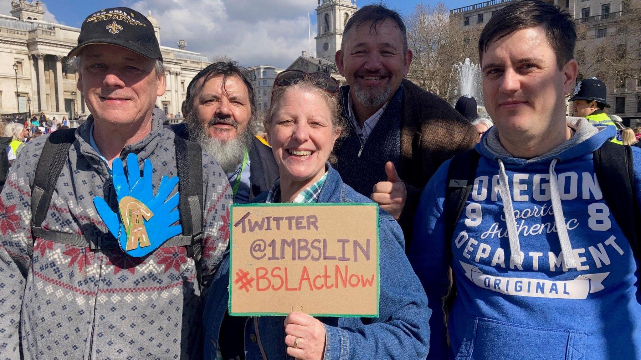 Some of the Portsmouth Deaf Club members on the BSL rally in Trafalgar Square in March 2022.  A woman is holding a sign with an X handle and #BSLActNow.