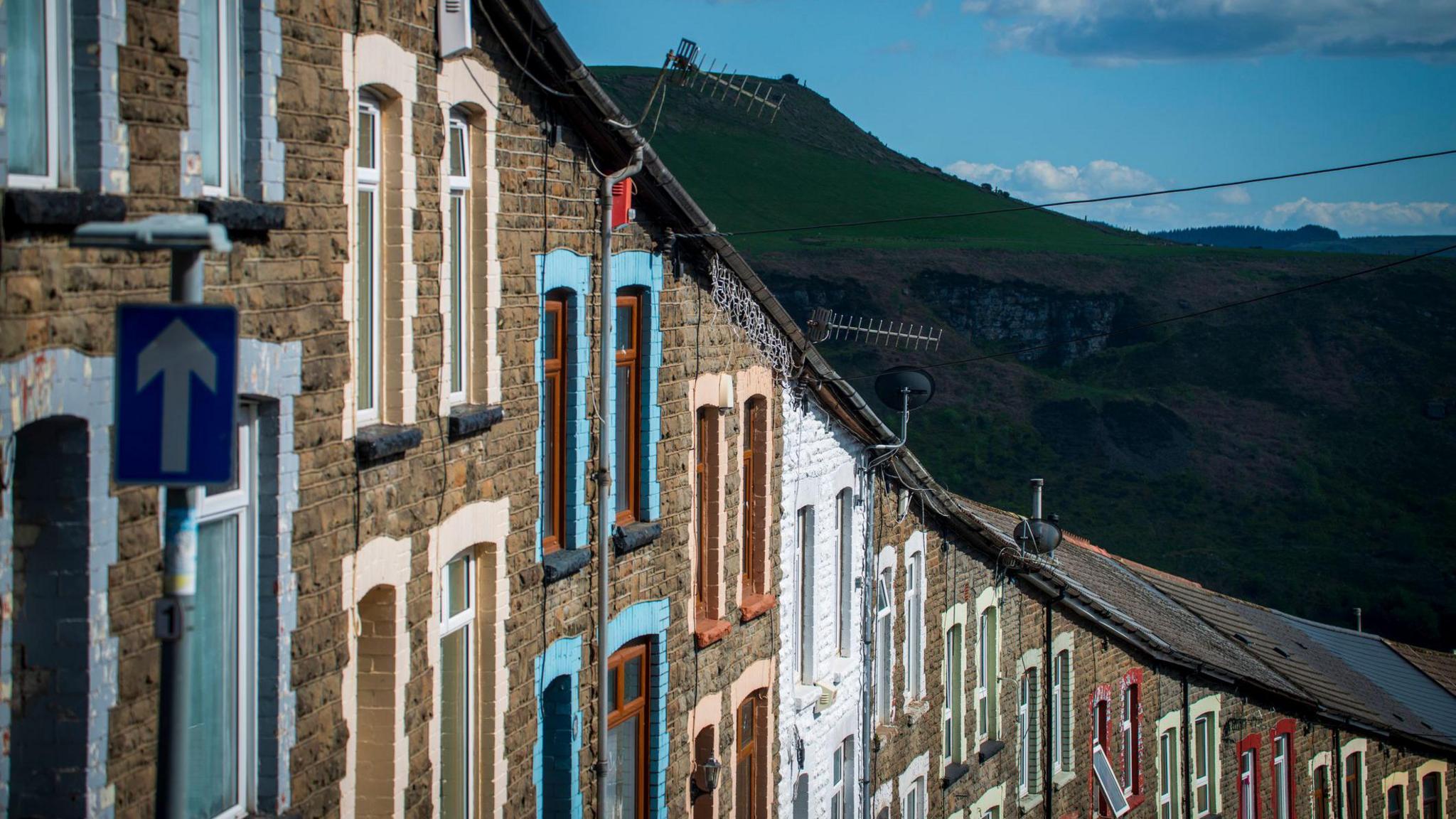 A row of terraced houses in a street in the Rhondda valley with a mountain in the background.
