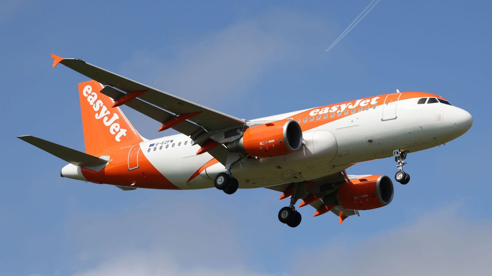 A white and orange EasyJet plane mid flight, pictured against a bright blue sky