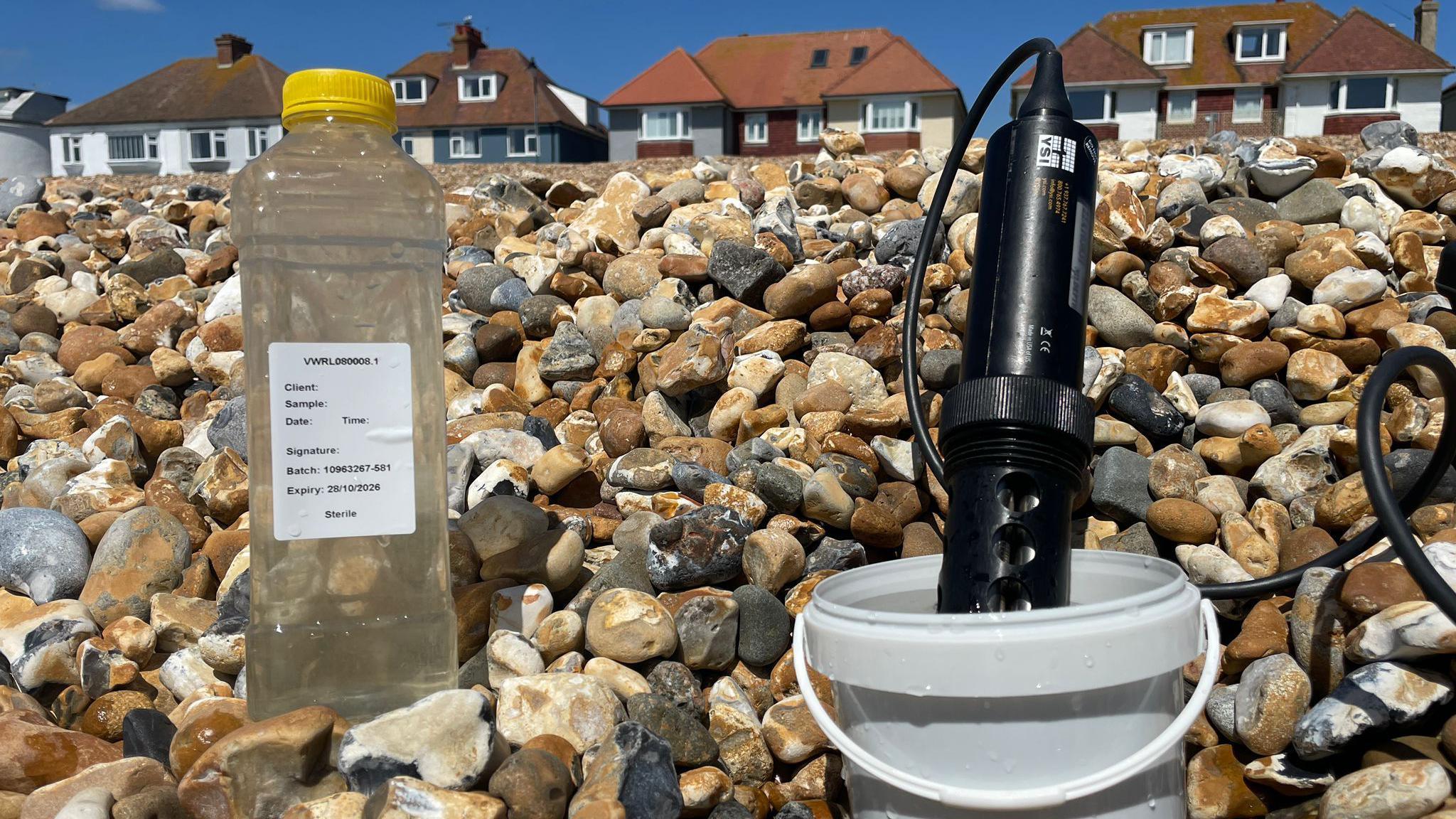 A plastic water bottle is full of seawater on a beach with a white label on it