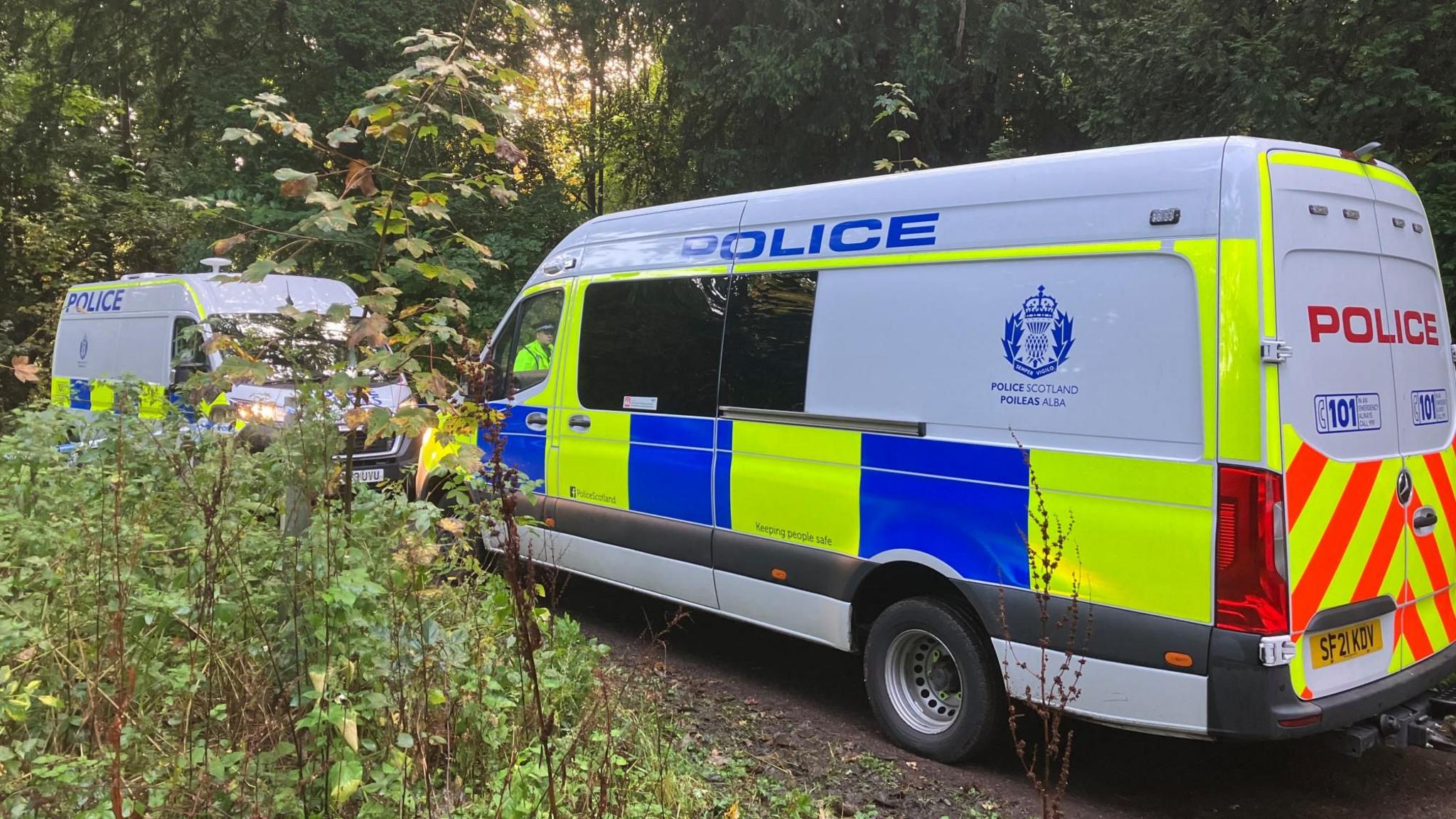 Two police van facing each other in a wooded area 