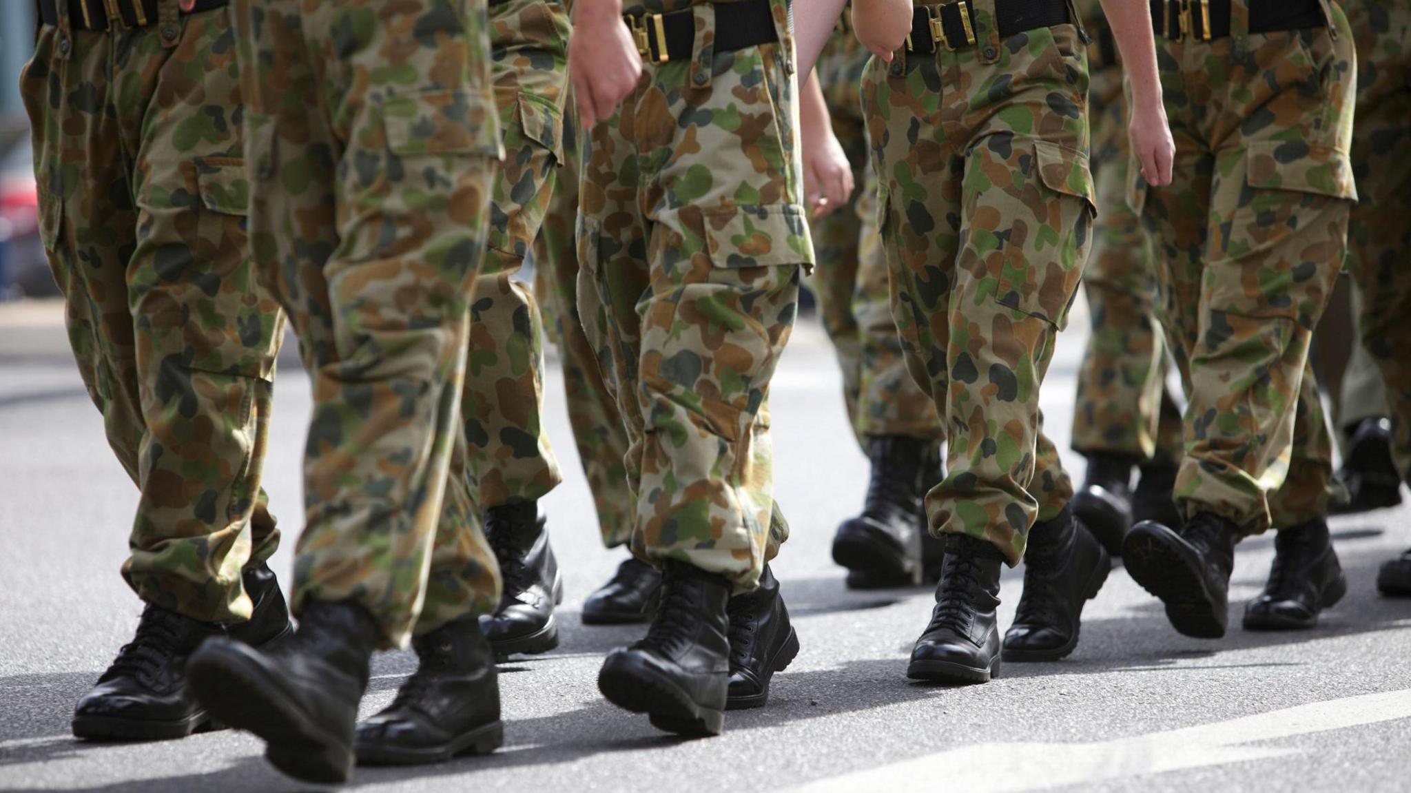 Several soldiers are seen from the waist down. They're wearing black boots and military camo fatigues trousers. 