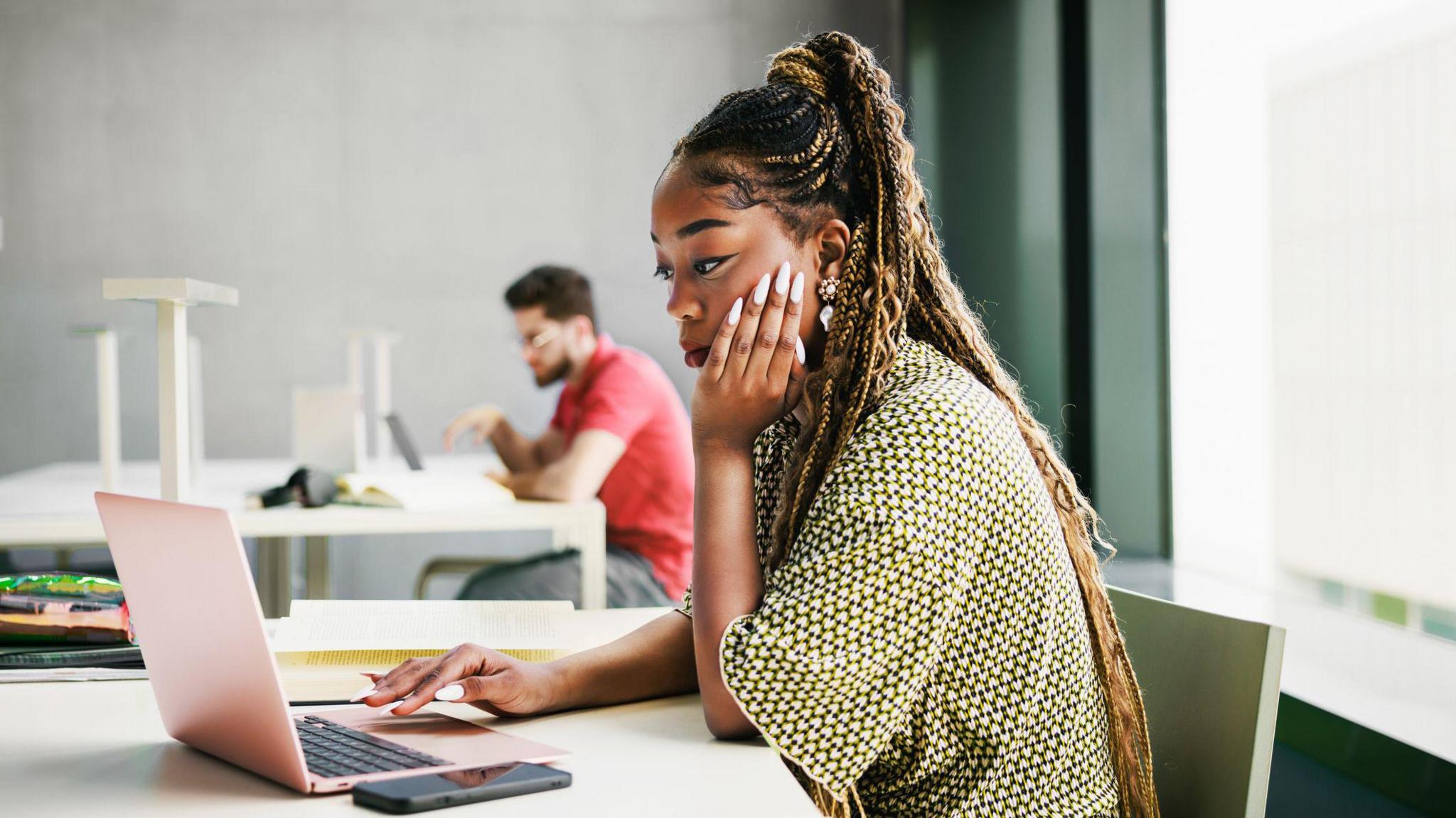 A woman with brown hair and a green top sat staring at a laptop