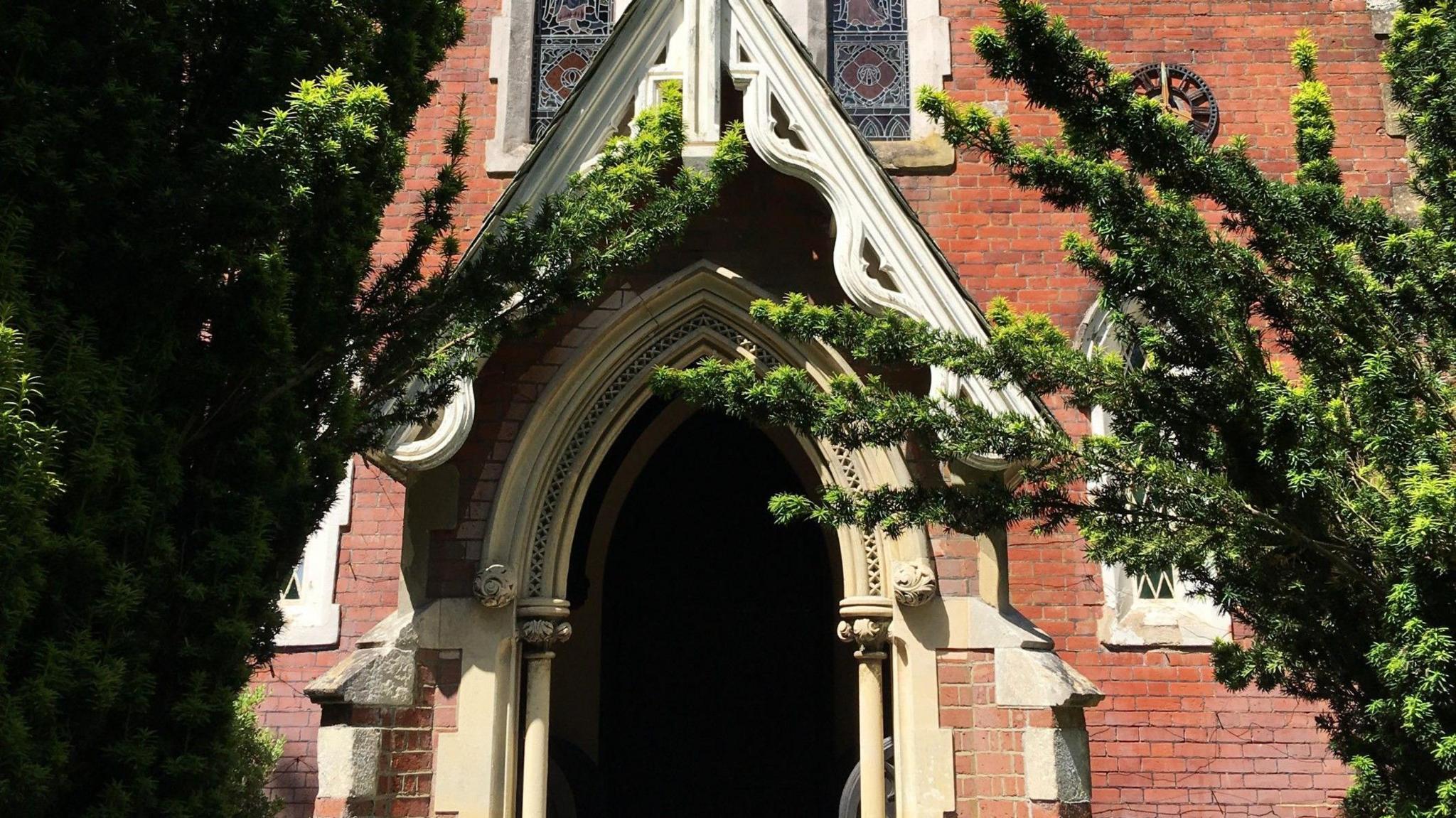 The main entrance to Longcross Church in Chertsey, showing the white stone archway and gabled roof, surrounded by the rest of the red brick building