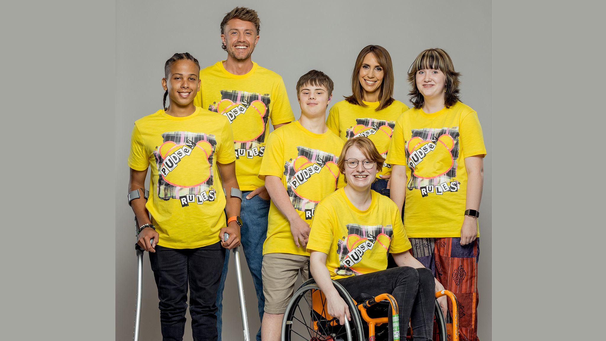 A group of six people - celebrities Alex Jones and Roman Kemp, with four youngsters, all wearing yellow Pudsey Bear T-shirts with a bear head and the words "Pudsey Rules" in punk-style print.
