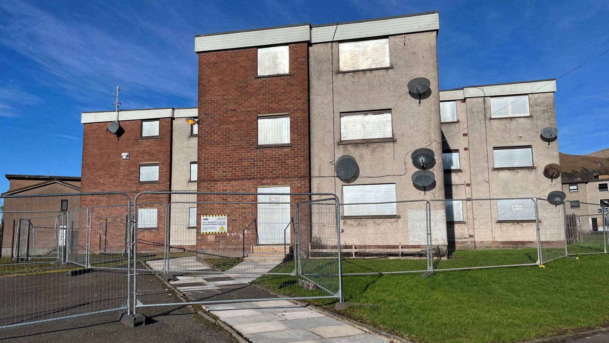 Exterior photo of a block of flats with a fence around the perimeter