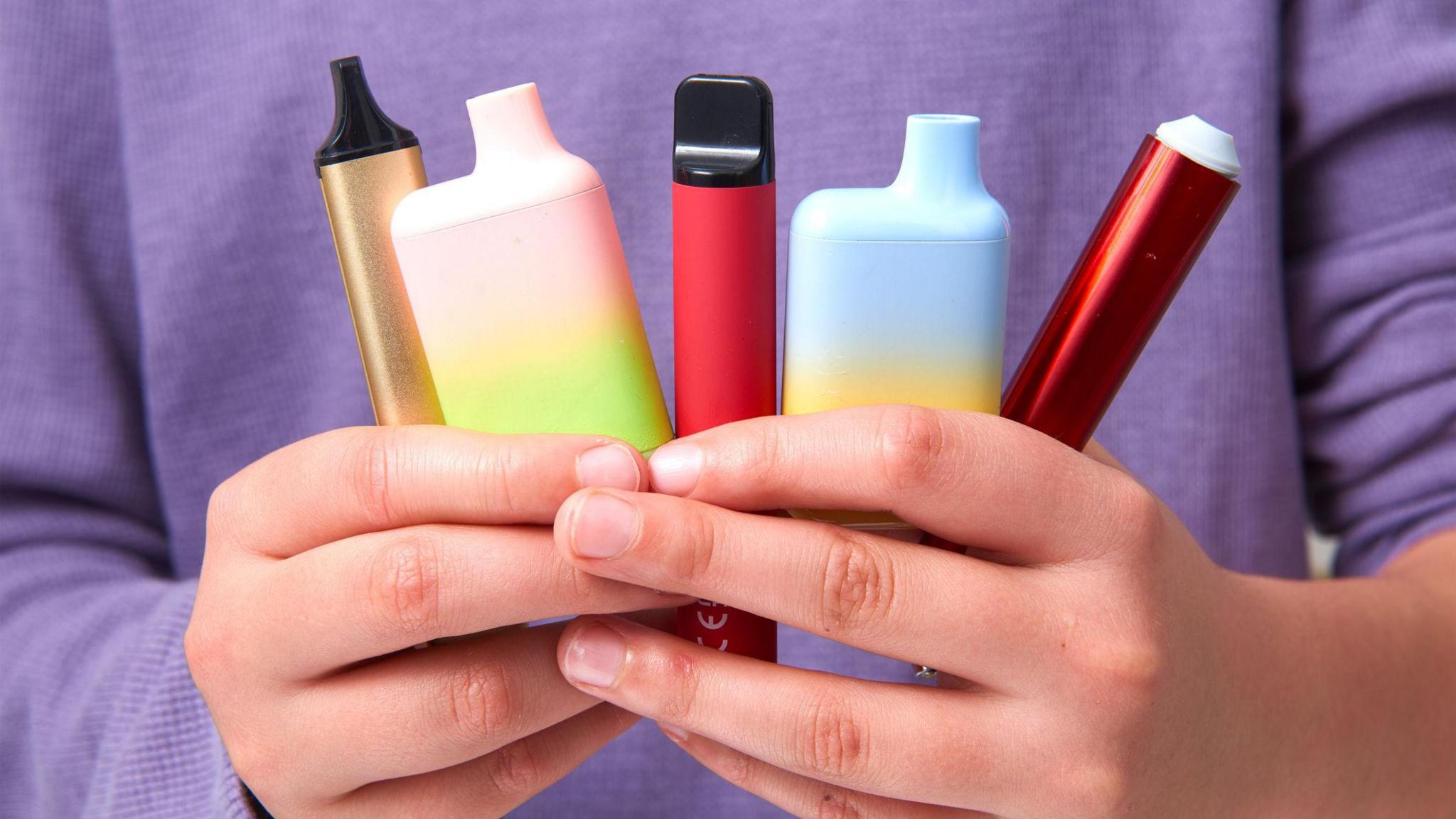 A young boy holding five colourful vapes