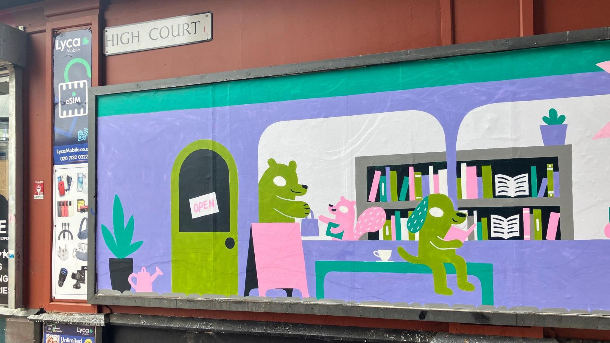 A vibrant mural painted on the side of a building depicts a whimsical indoor scene with cartoon-style animal characters. A green bear sits at a pink desk near a door marked 'OPEN,' while a pink squirrel stands nearby holding a book. To the right, a green dog reads at a purple table. Behind them are colourful bookshelves and potted plants. The mural is located on a building with a street sign above that reads 'HIGH COURT'.