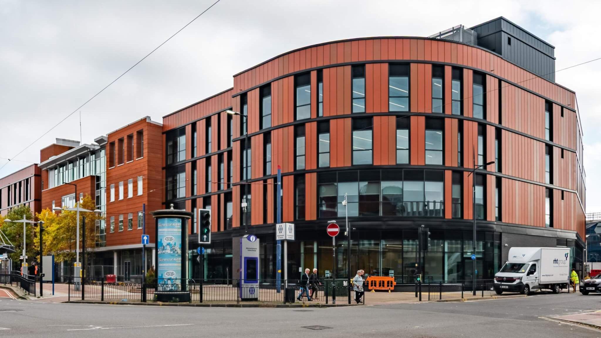 A large orange-coloured round building with glass window panels around it on a street. There are road signs around it and vehicles on the road outside.