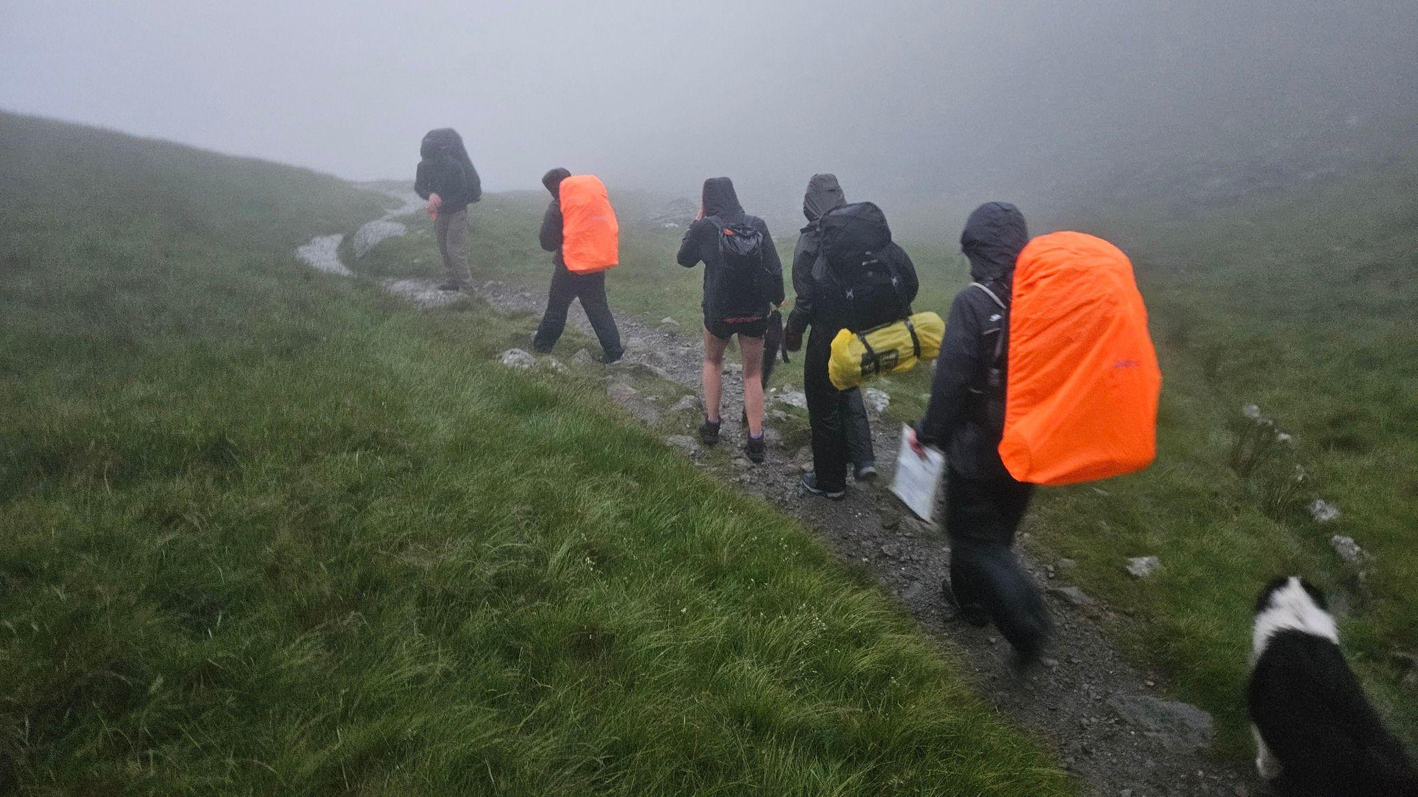 A group of DofE students wearing large hiking rucksacks walk in a drizzly wet environment in the Lake District.