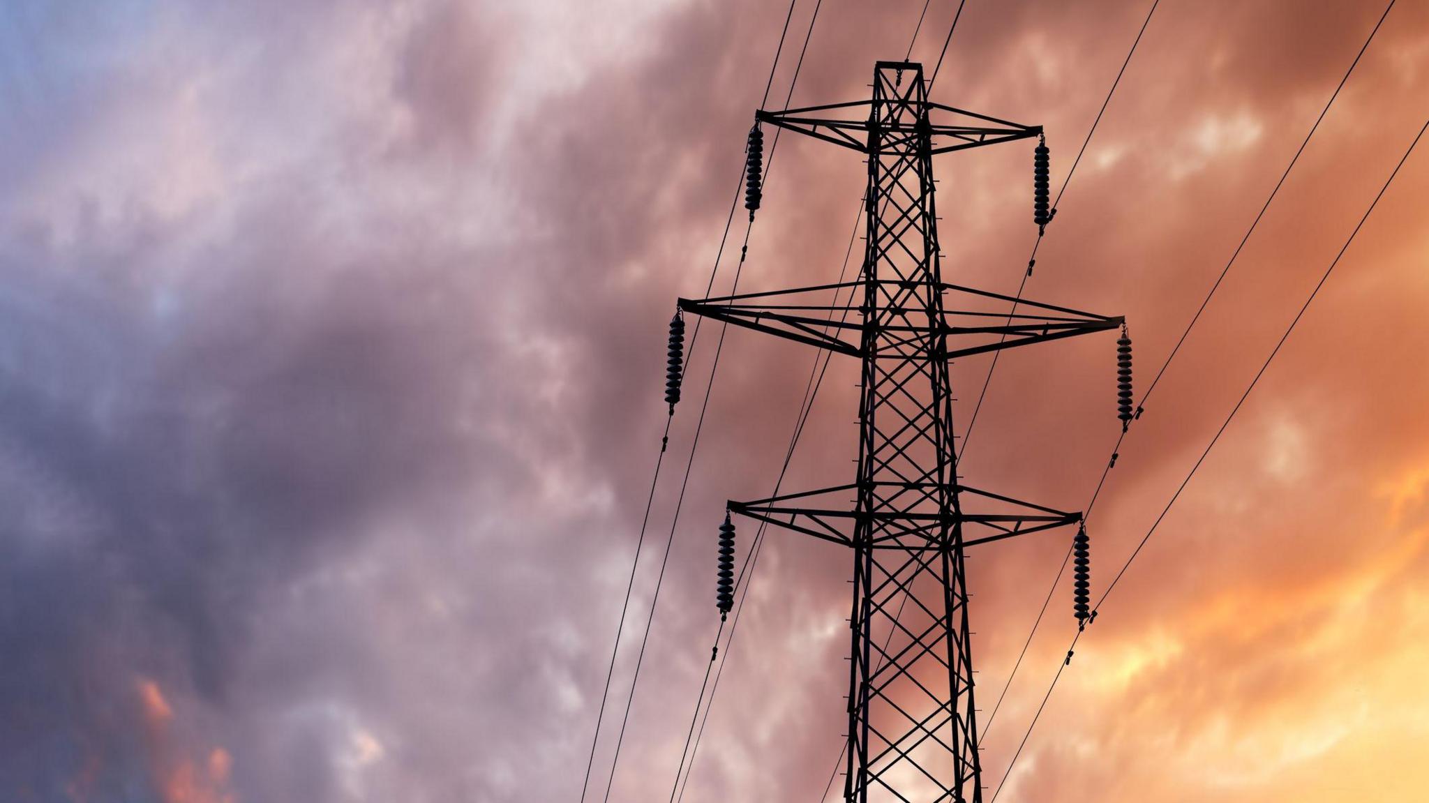 A British Style Electricity Pylon and suspended electic cables against a Blue Cloudy Sky