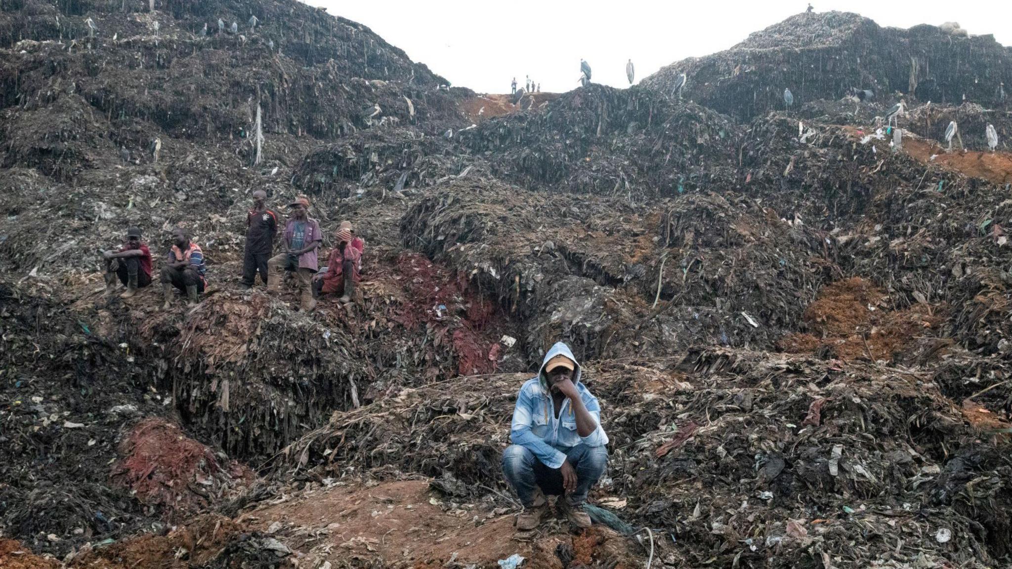 A man sits surrounded by huge piles of rubbish in Kampala on August 10, 2024. 