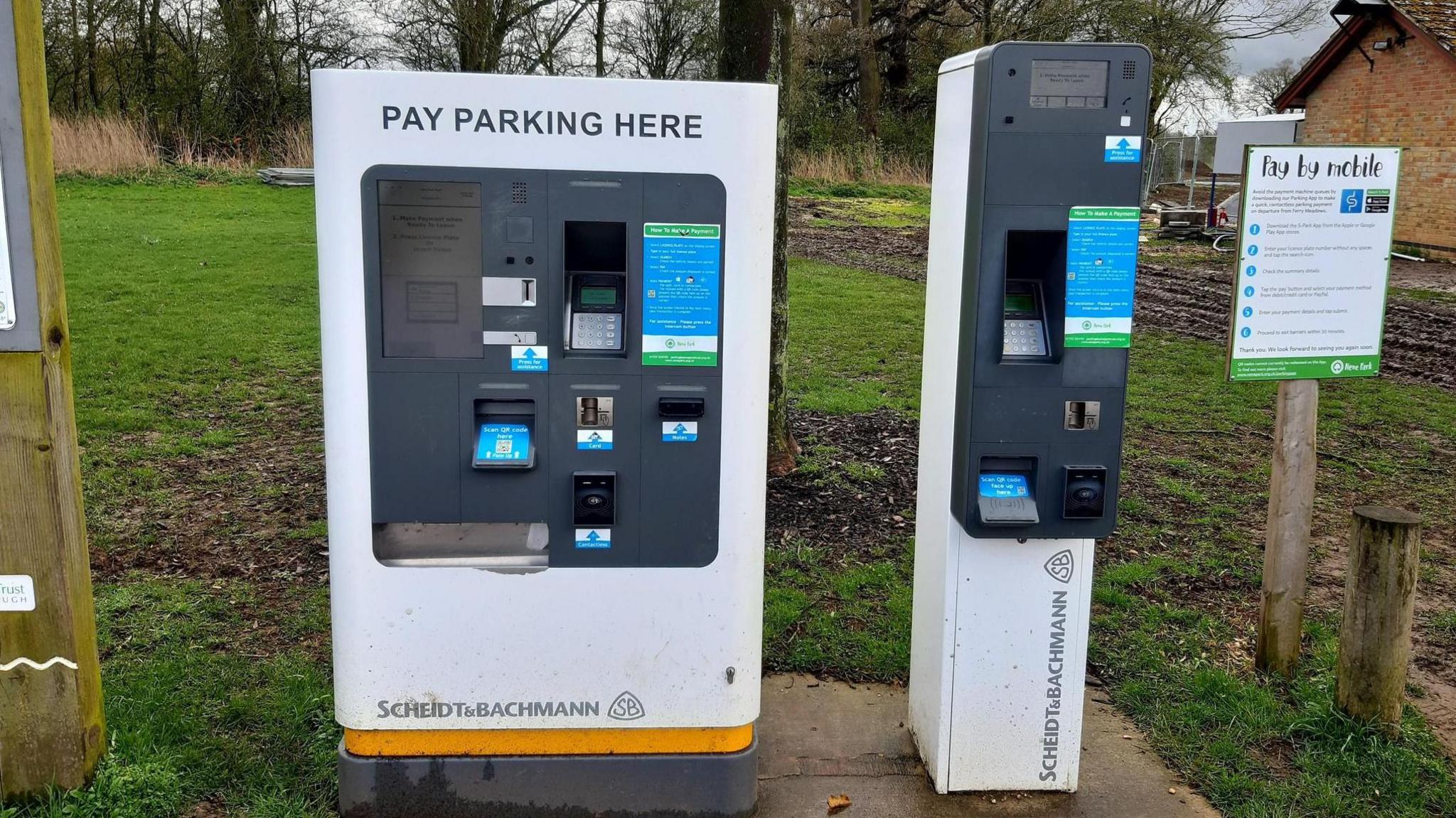 White and grey rectangle parking machines with a digital display screen and a 'pay by mobile' sign board next to it 