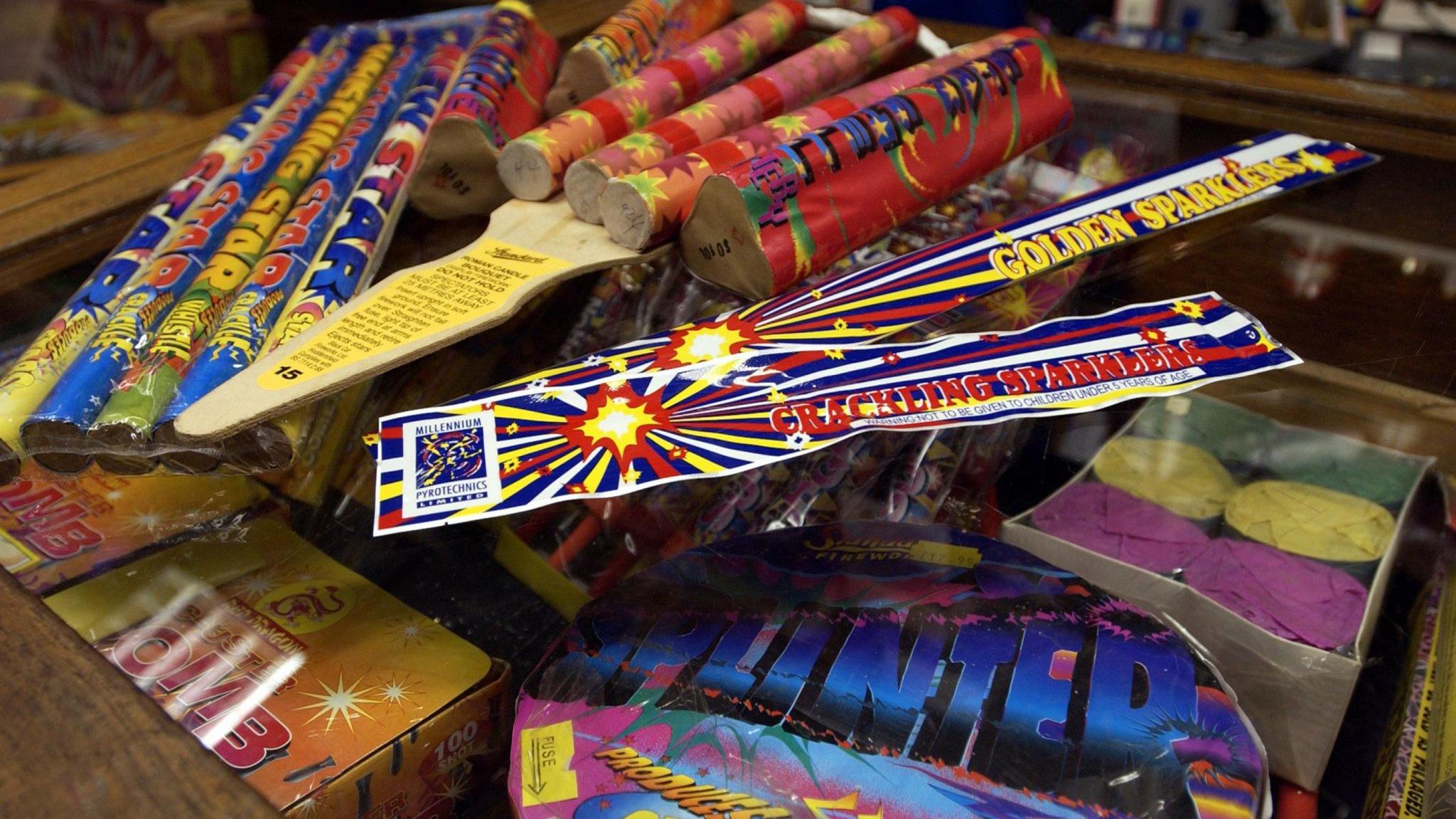An array of brightly coloured  red, yellow and blue packets of firework, including sparklers and what appear to be rockets,