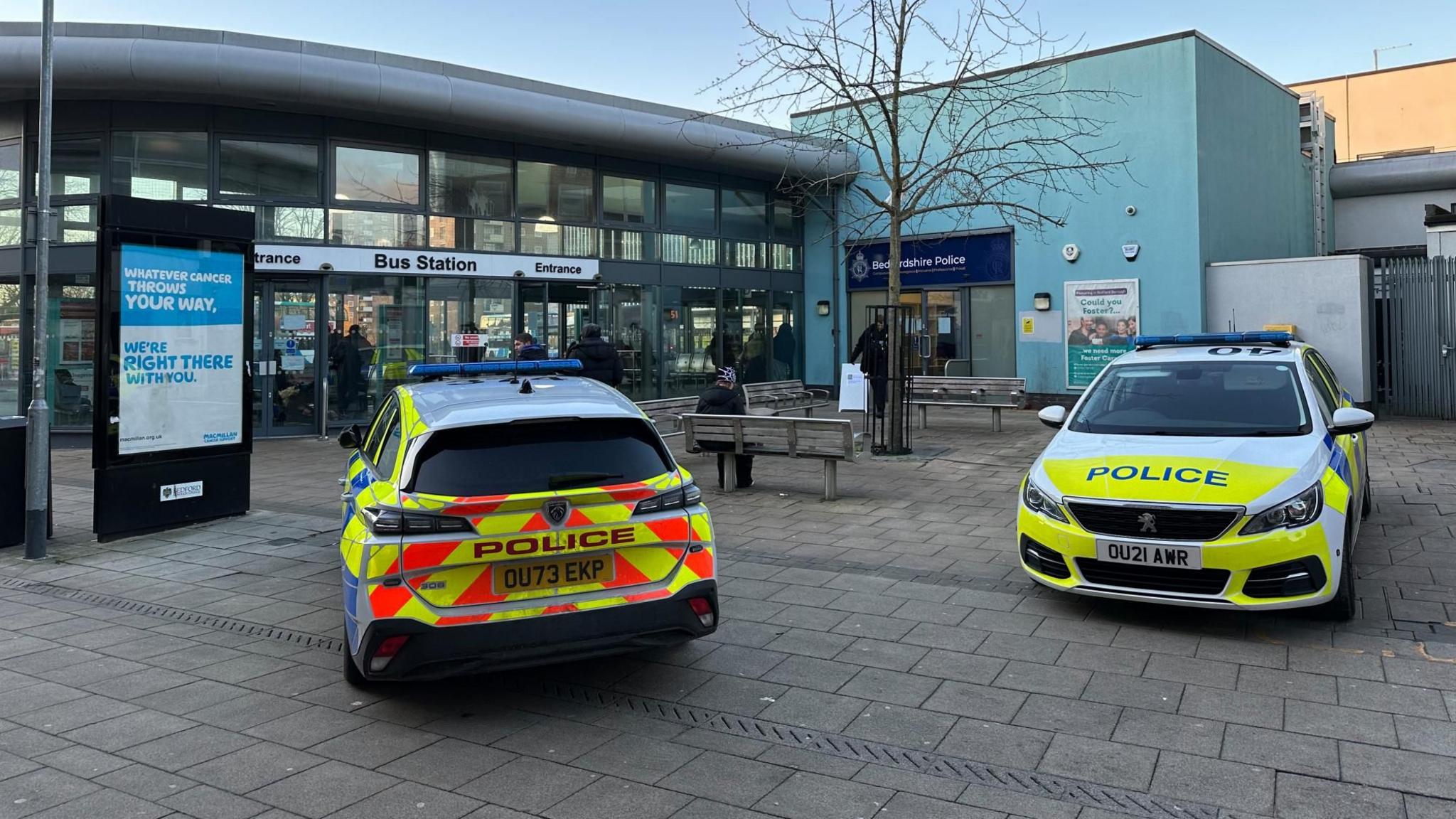 Two police cars parked on the pavement outside Bedford bus station. There is a police station next to the bus station, and the entrance to the police station is in the shot.