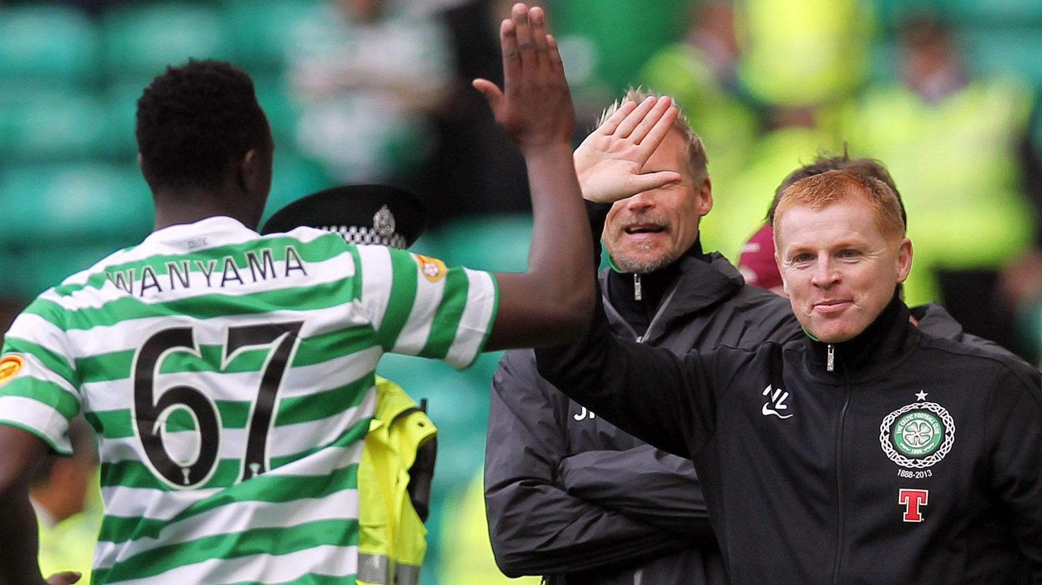 Victor Wanyama, seen from behind wearing a green and white striped Celtic shirt with the number 67 on the back, approaches manager Neil Lennon for a high five