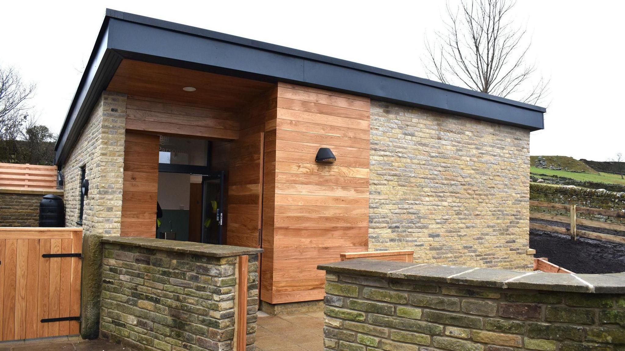 A toilet block building in stone and brown wood panels.