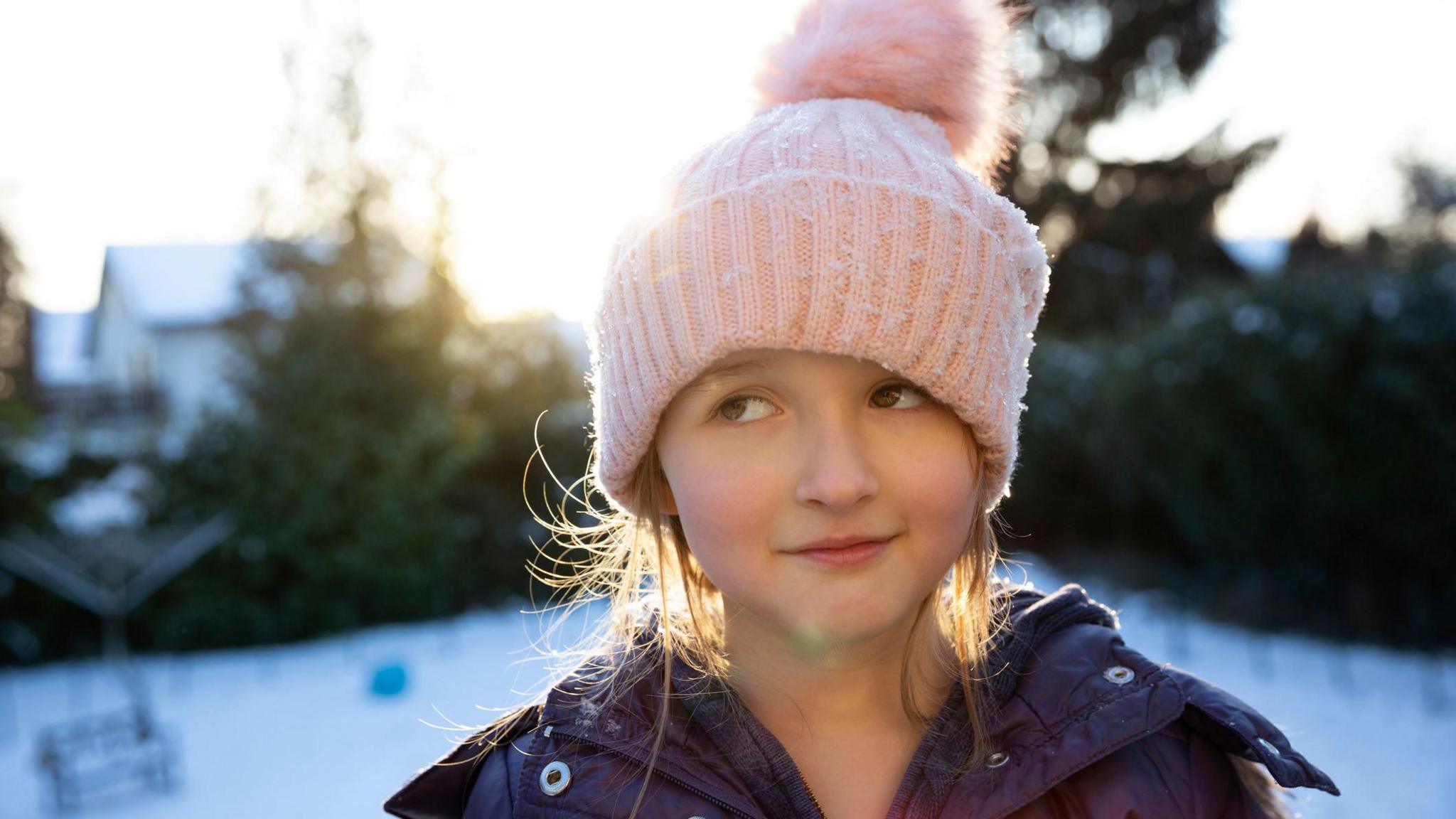A child with a quizzical look in hat and gloves outside.