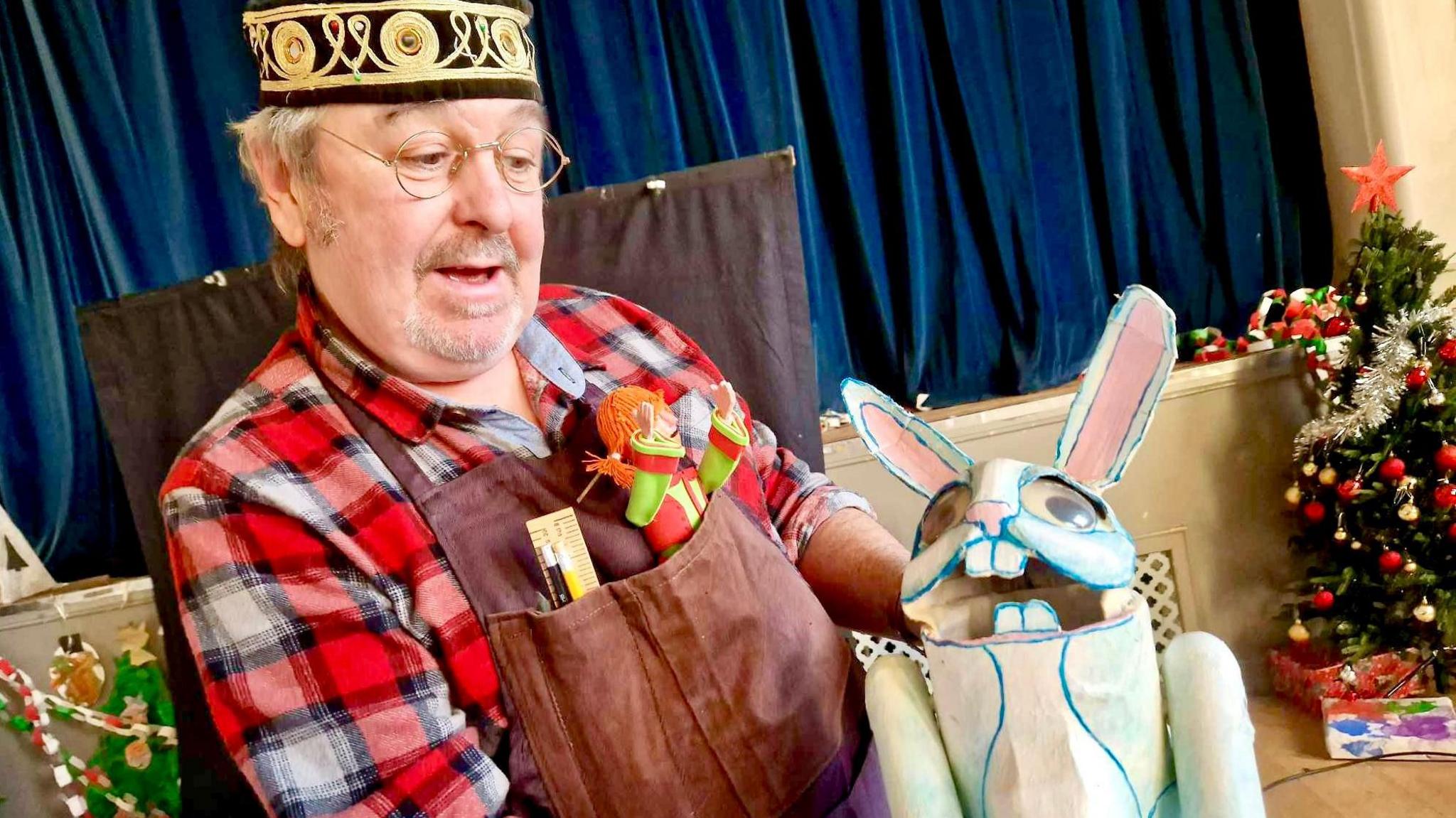 Paul in a community hall looking at a white rabbit puppet made out of carboard.