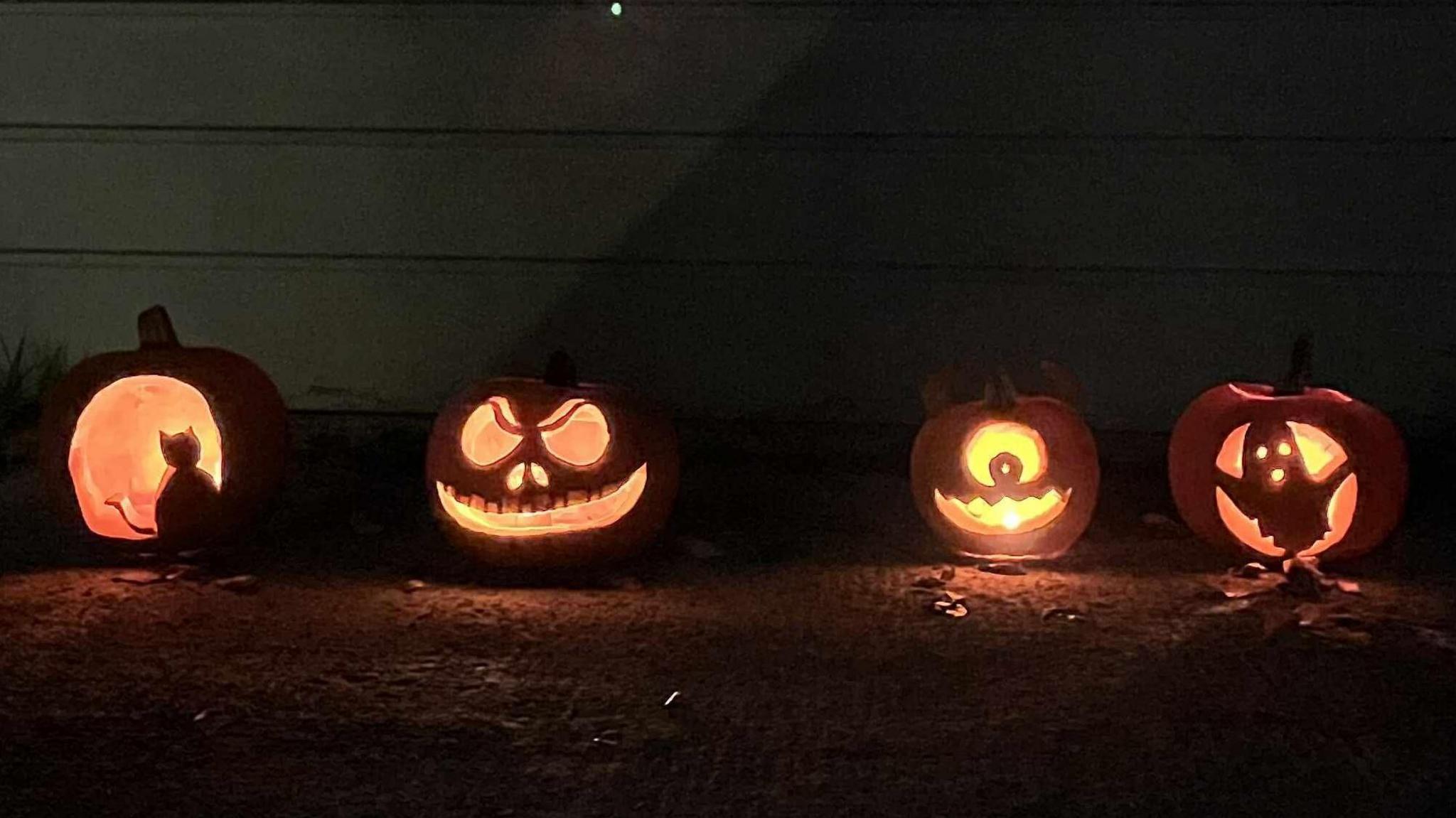 Four carved orange pumpkins with different patterns, lit from the inside by candles