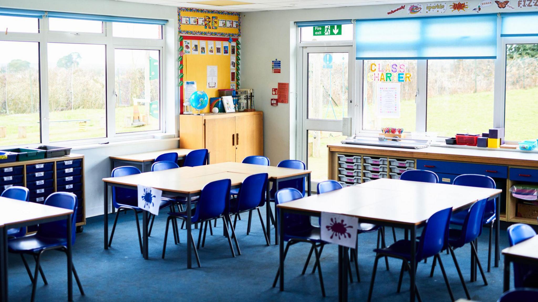 an empty classroom with blue chairs around wooden tables