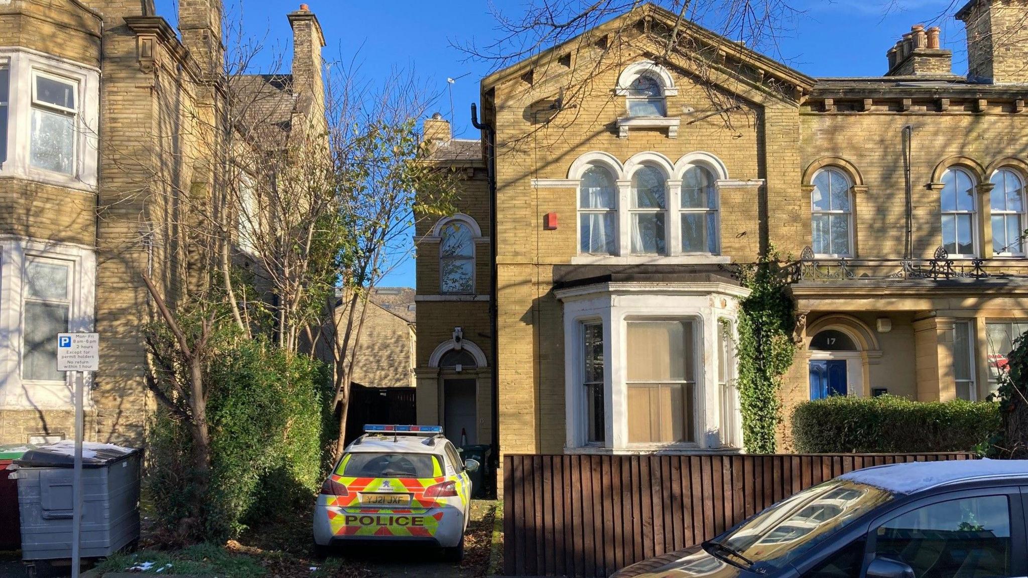 A police car parked in the short driveway of the stone-built, three-storey end of terrace Victorian terrace.