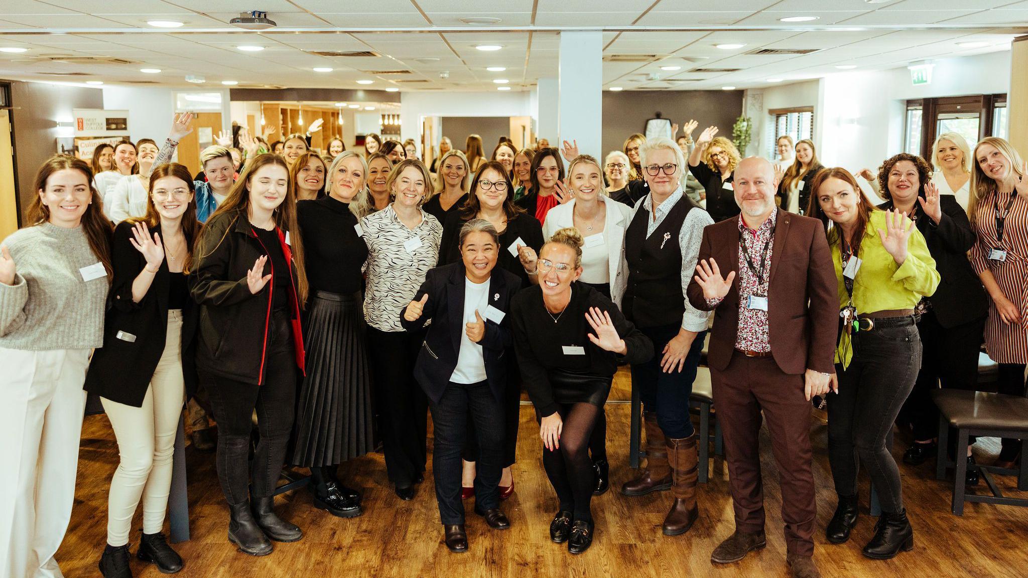 The guests of the Construction Anglia event. They are in a room pictured in a close group facing the camera. They each are waving to the camera with smiles on their faces.