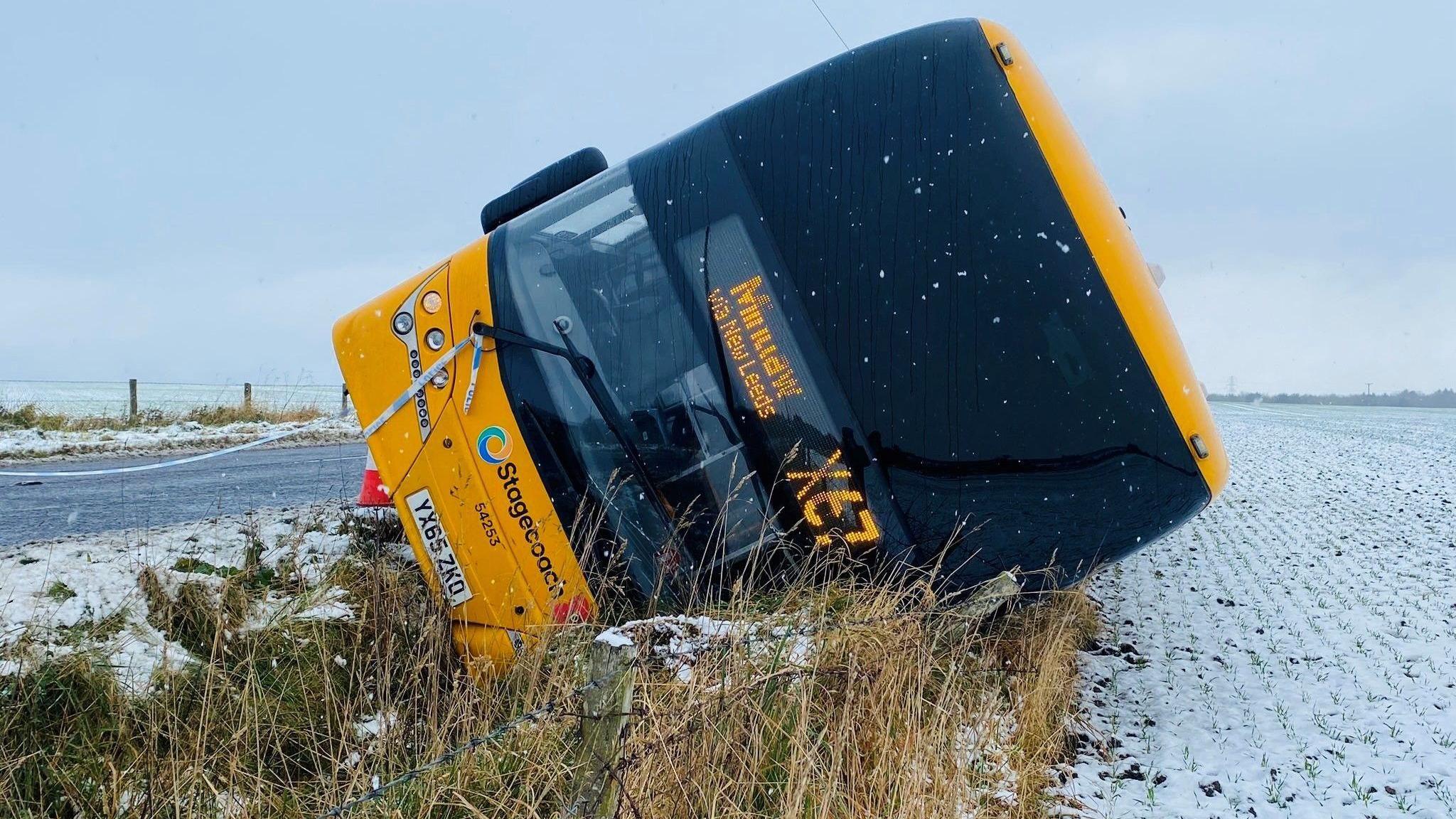 Yellow Stagecoach bus on side at side of road, next to a snow-covered field.