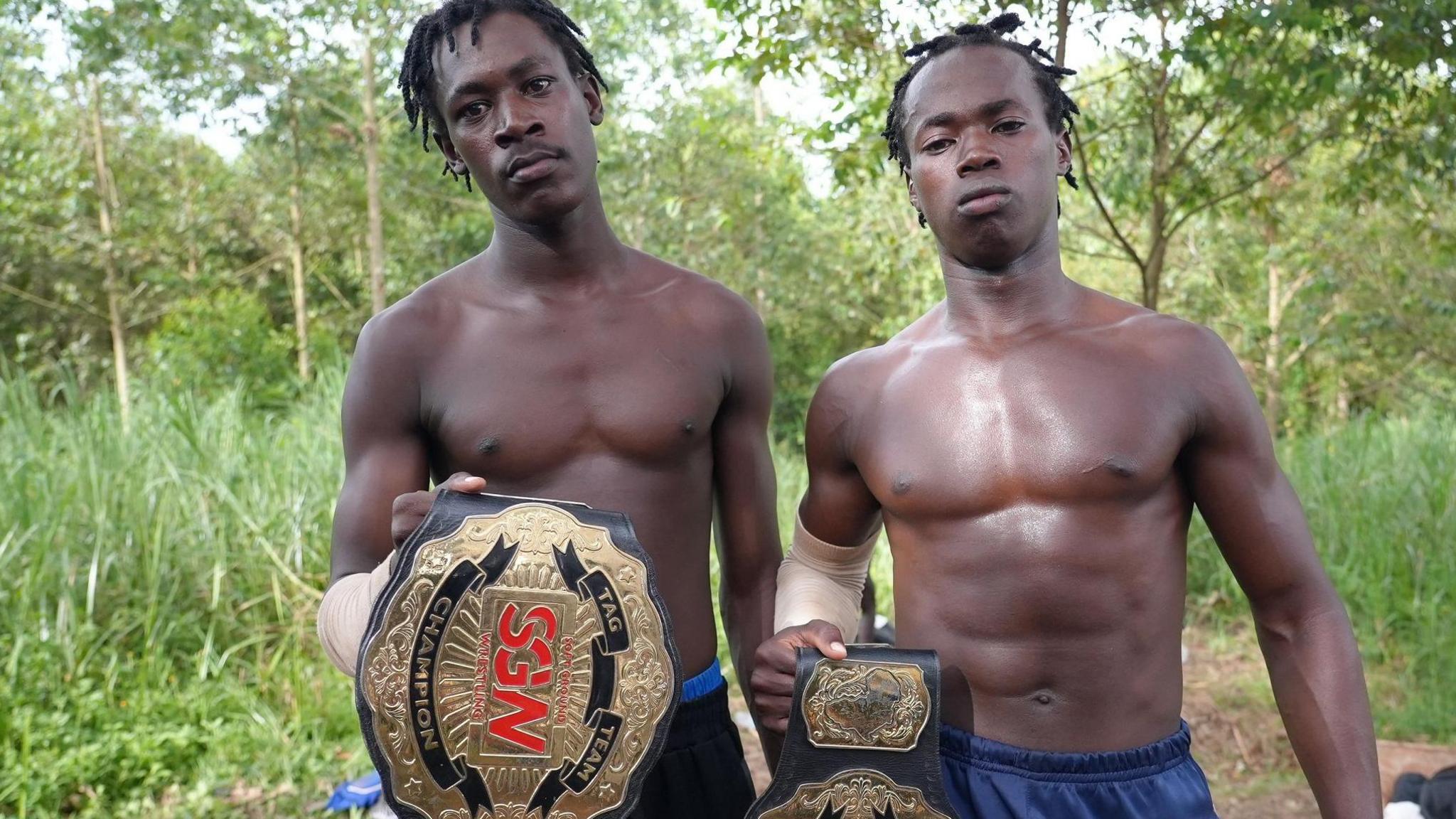 Two men pose shirtless while holding SGW wrestling belts