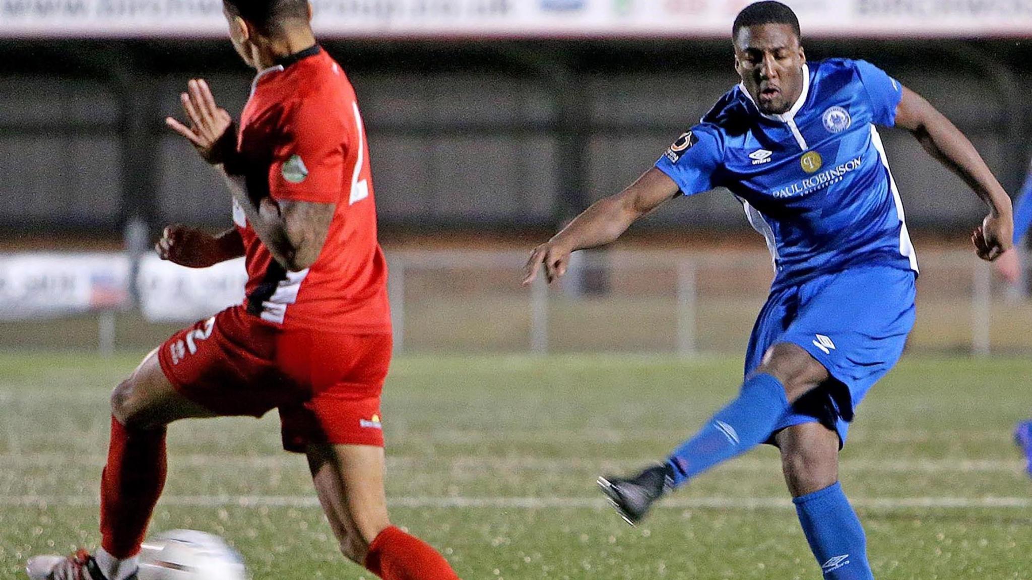 On the right of the image Devonte is dressed in a blue Billericay Town football kit as he tries to intercept another player, seen from behind, wearing a red kit.