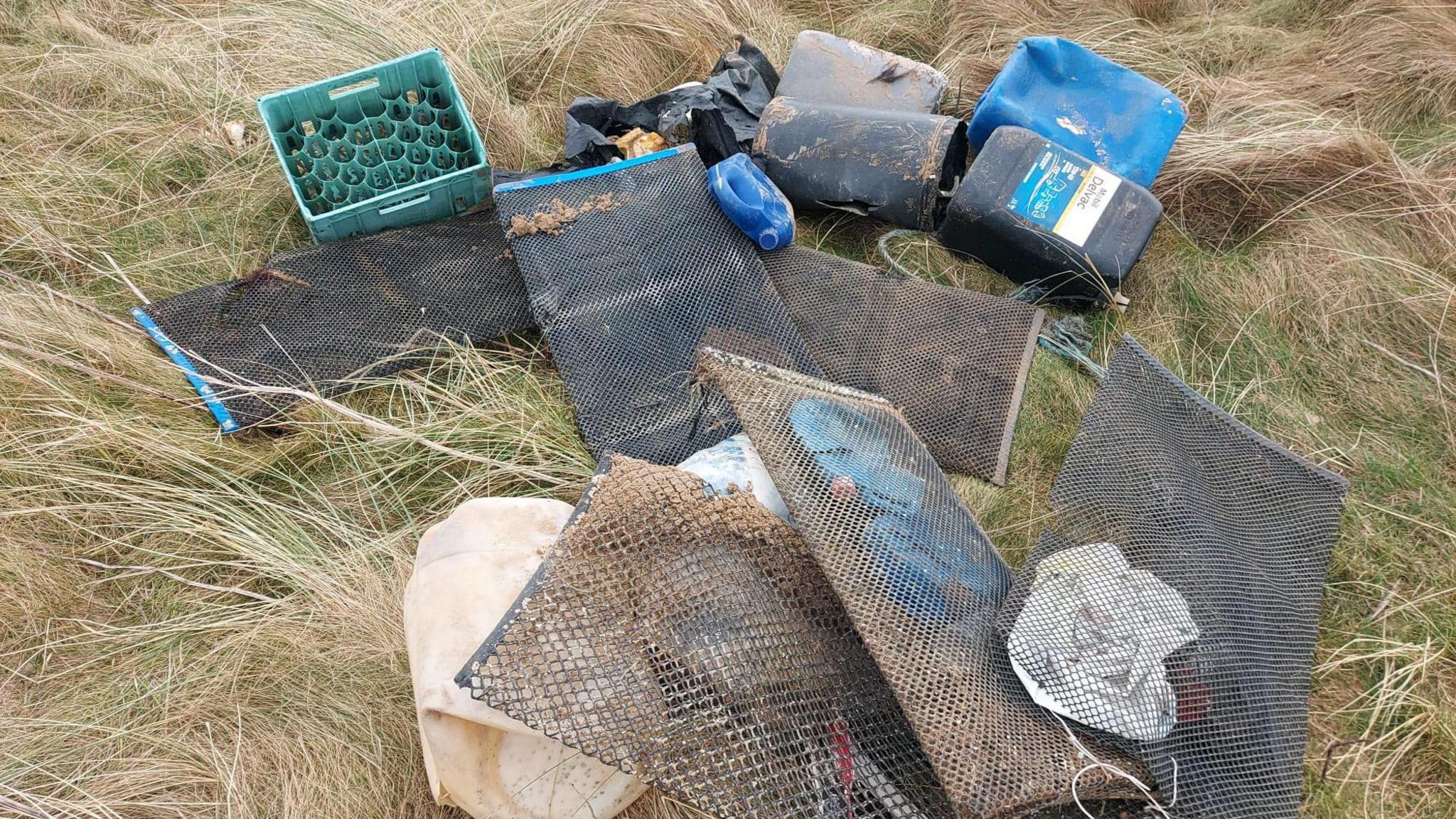 An image of an assortment of rubbish - including plastic containers, a plastic crate and pieces of wire mesh lying on a piece of grassy ground