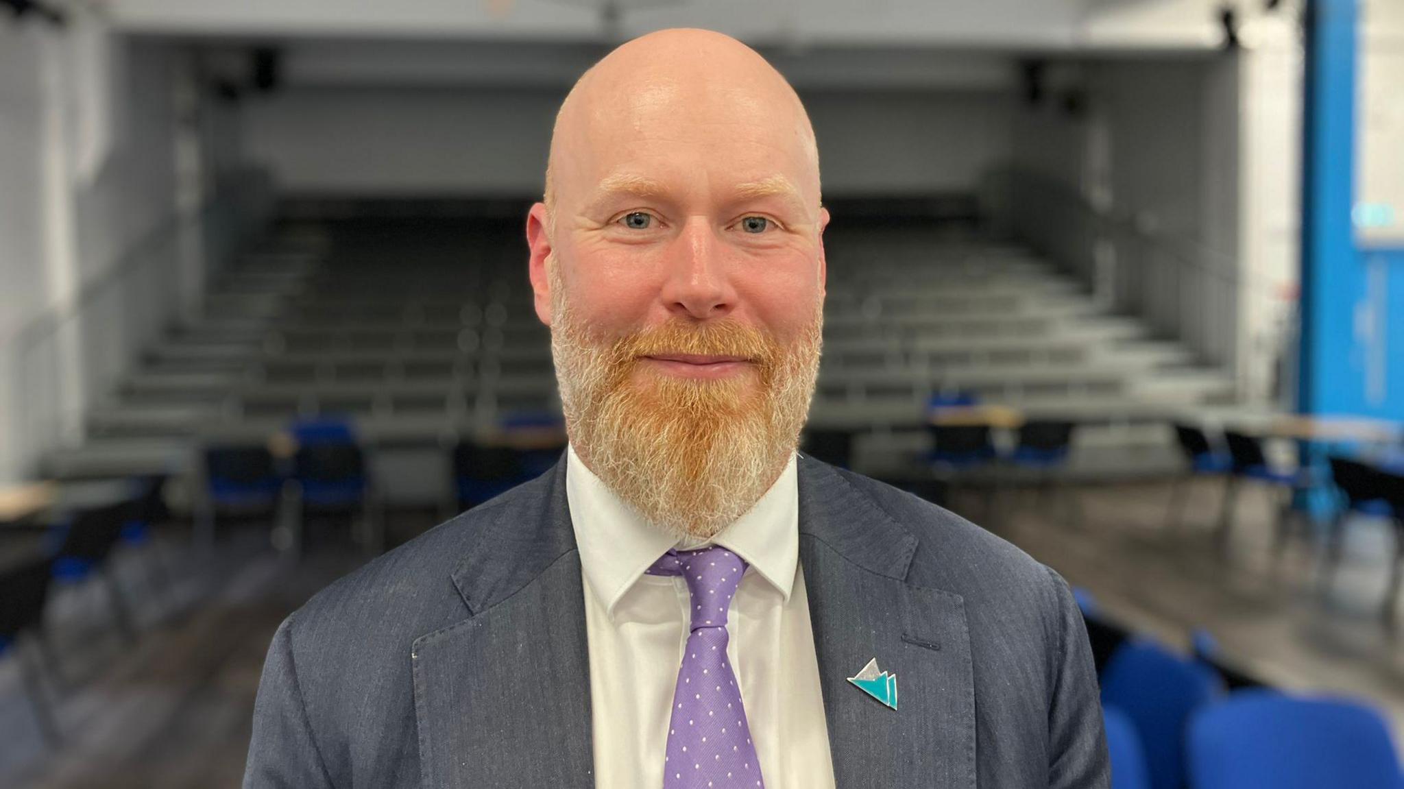 Alex Hughes standing in a school hall and smiling at the camera