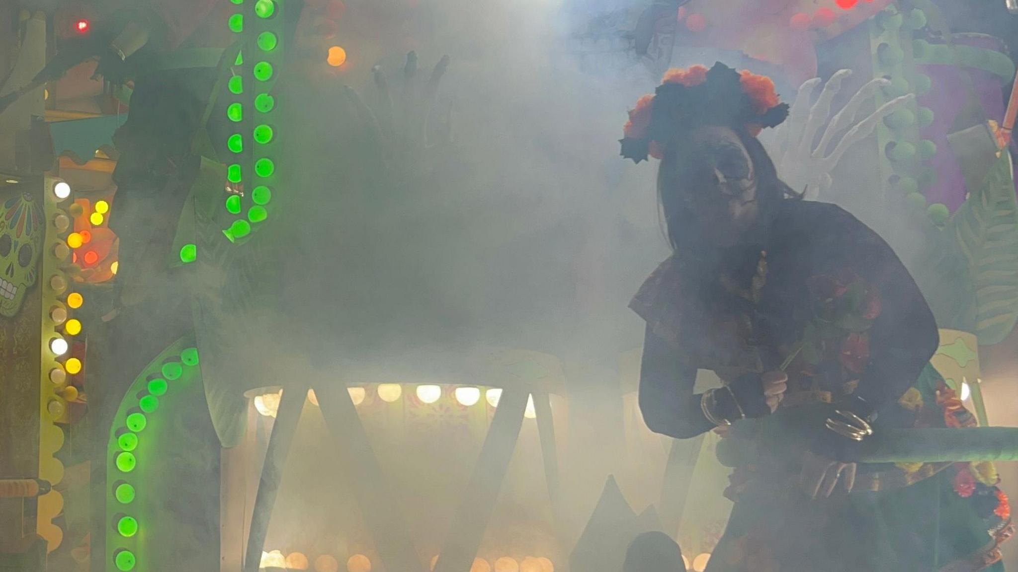 A costumed performer on a carnival cart. She is wearing face paint and a flower crown.